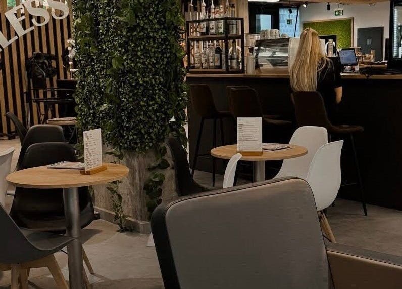 Интерьер кафе в Barber KRVTSV, Hlavní Město Praha, CZ с уютными столиками и зеленью.