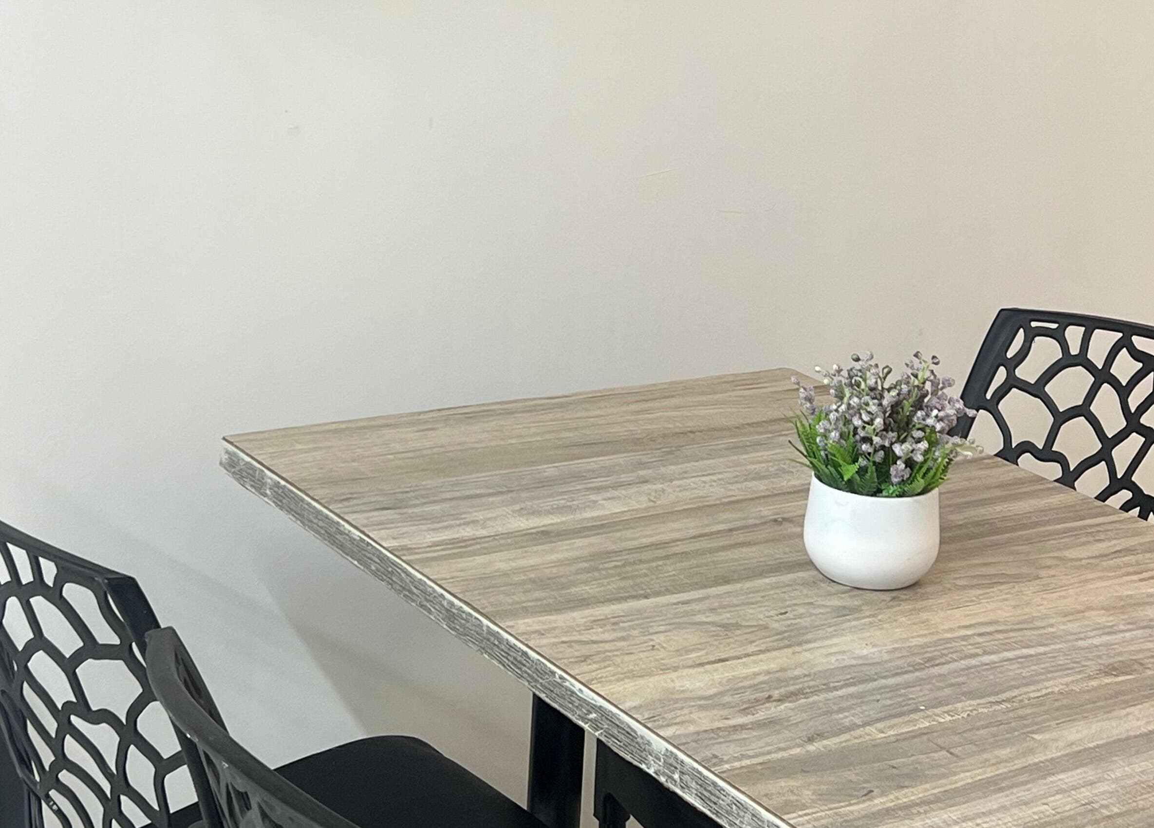 Mesa decorativa en Aura Nails Spa, Caldas, Caldas, CO con sillas negras y planta ornamental.