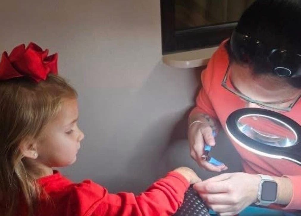 Young girl receives a manicure at Layered & Linked, Madisonville, Tennessee, US, under bright lamp.