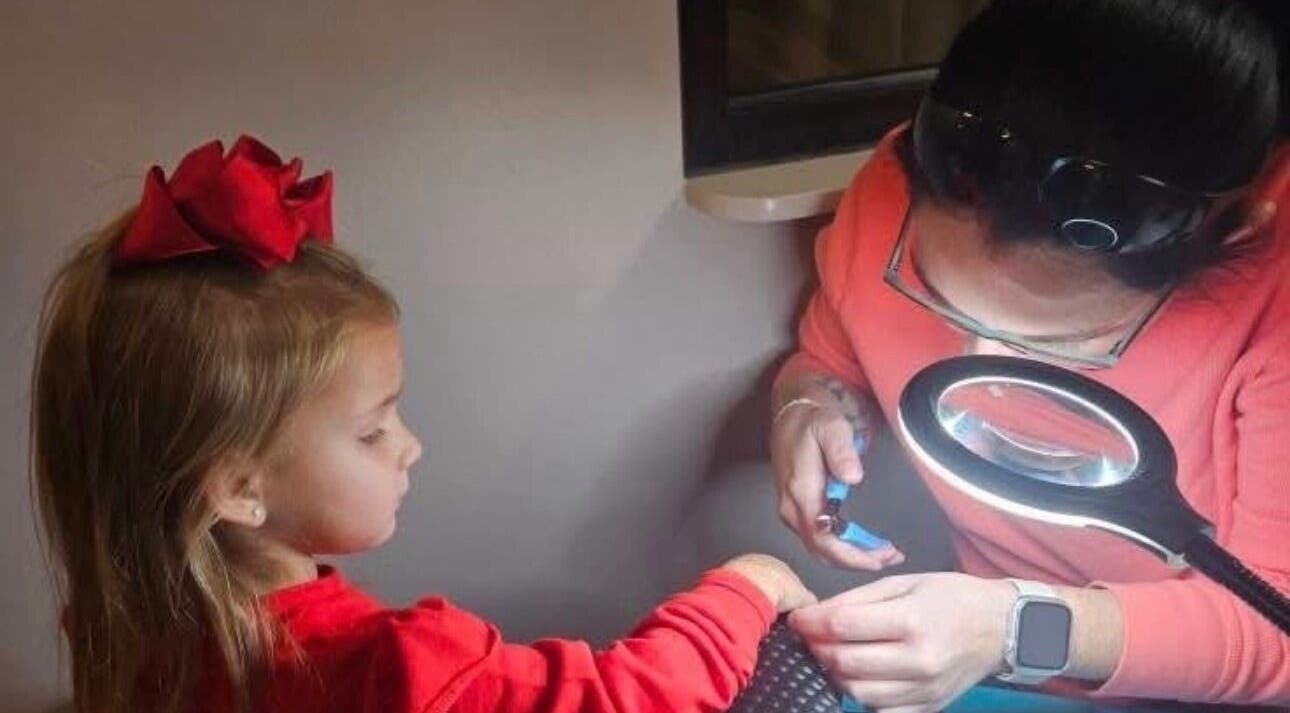 Young girl receives a manicure at Layered & Linked, Madisonville, Tennessee, US, under bright lamp.