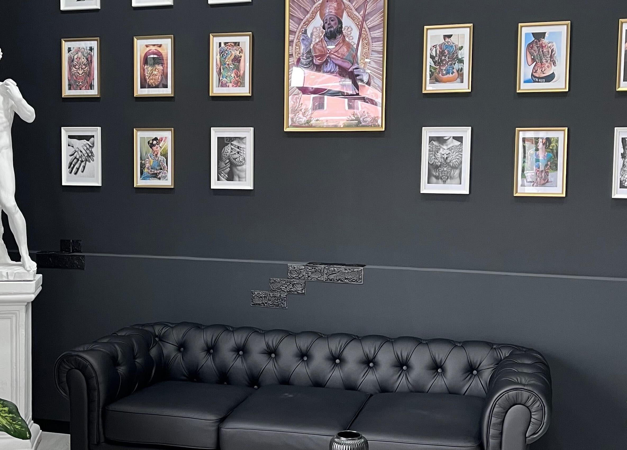 Interno di Got Ink Tattoo a Marzanello, Campania, con divano nero e statue d'arte classica.