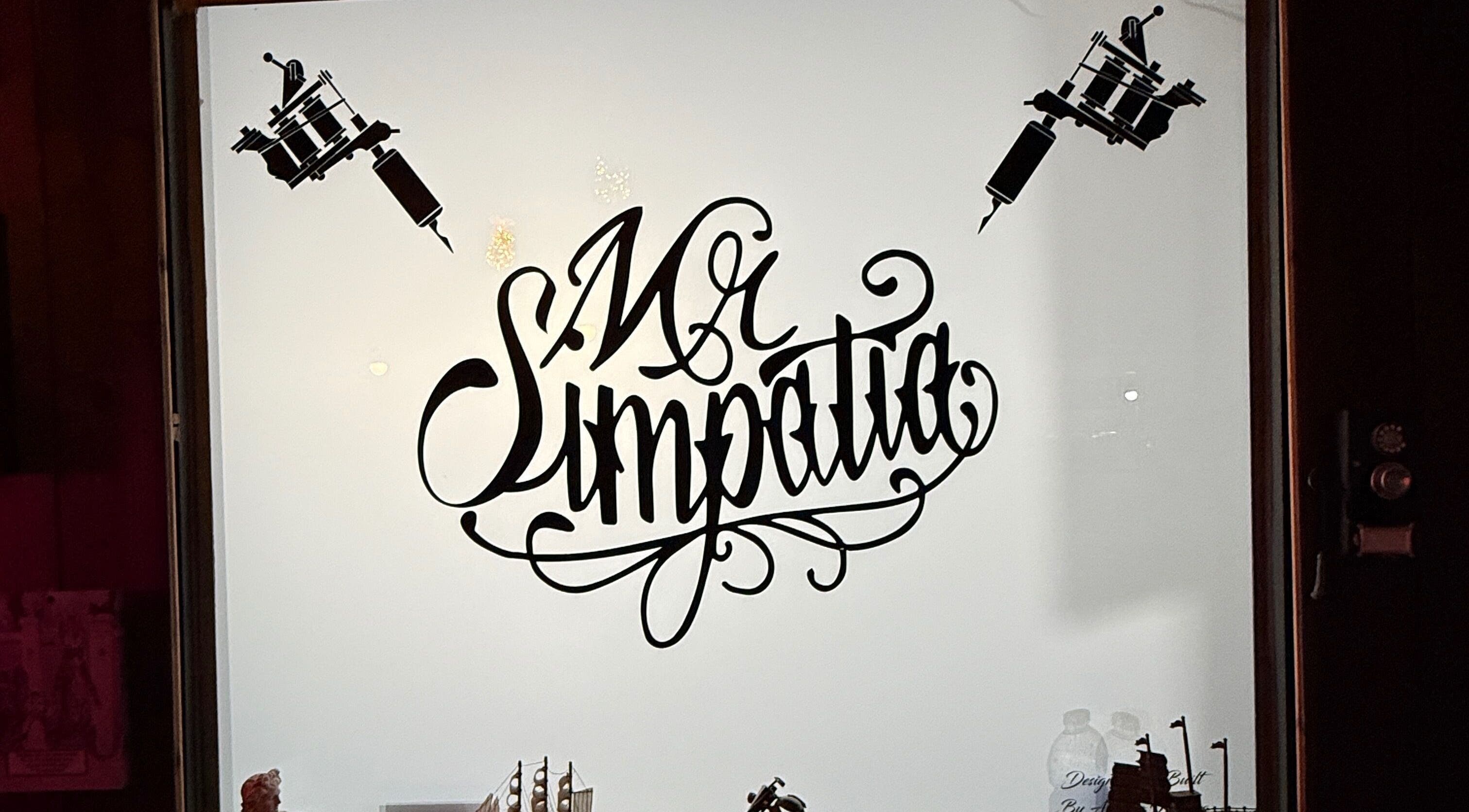 Logo del Mr Simpatia Tattoo Studio a Mondragone, Campania, IT, su una vetrina illuminata.