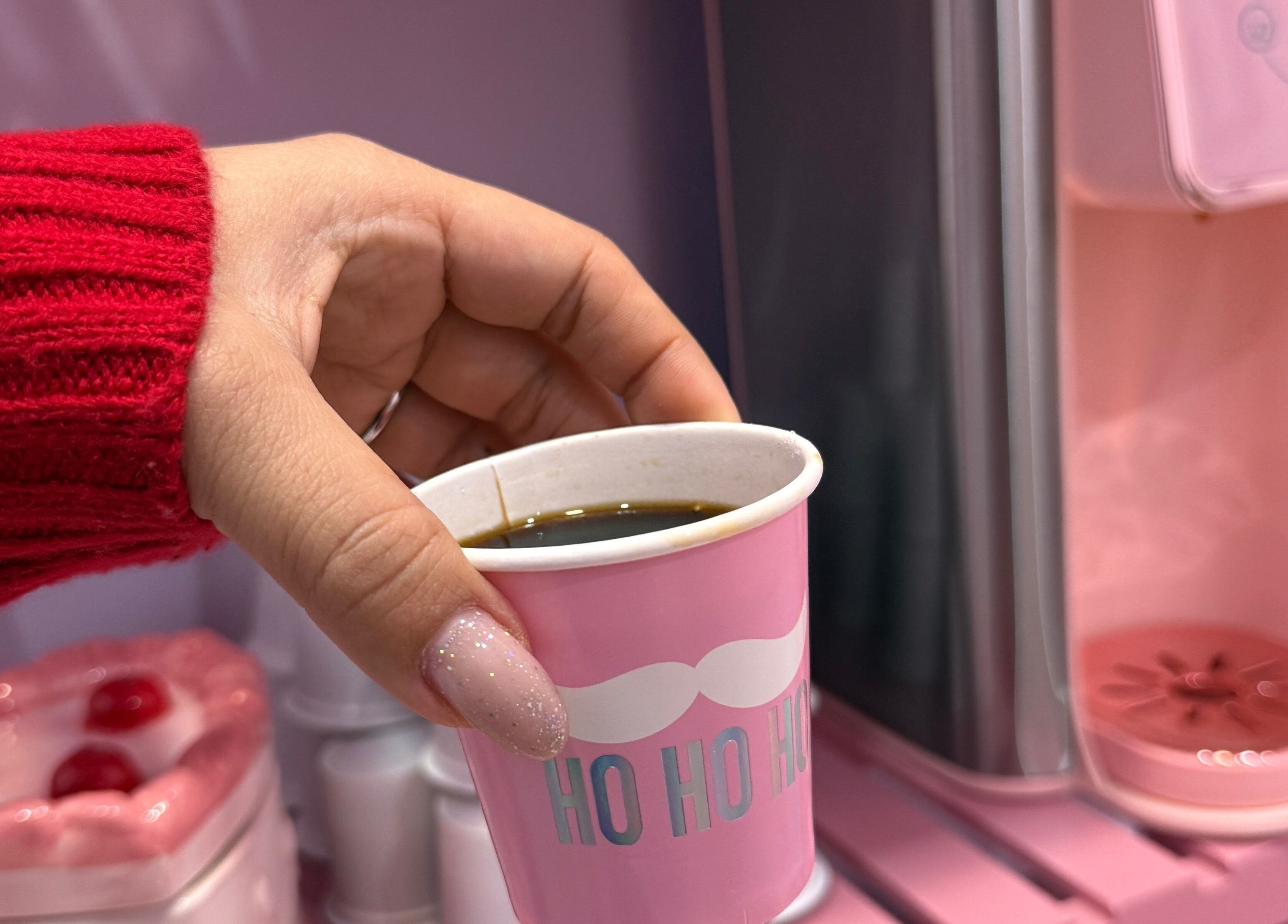 Hand holding pink cup of coffee at The Nail Room, Hialeah, Florida, US, against a stylish pink background.