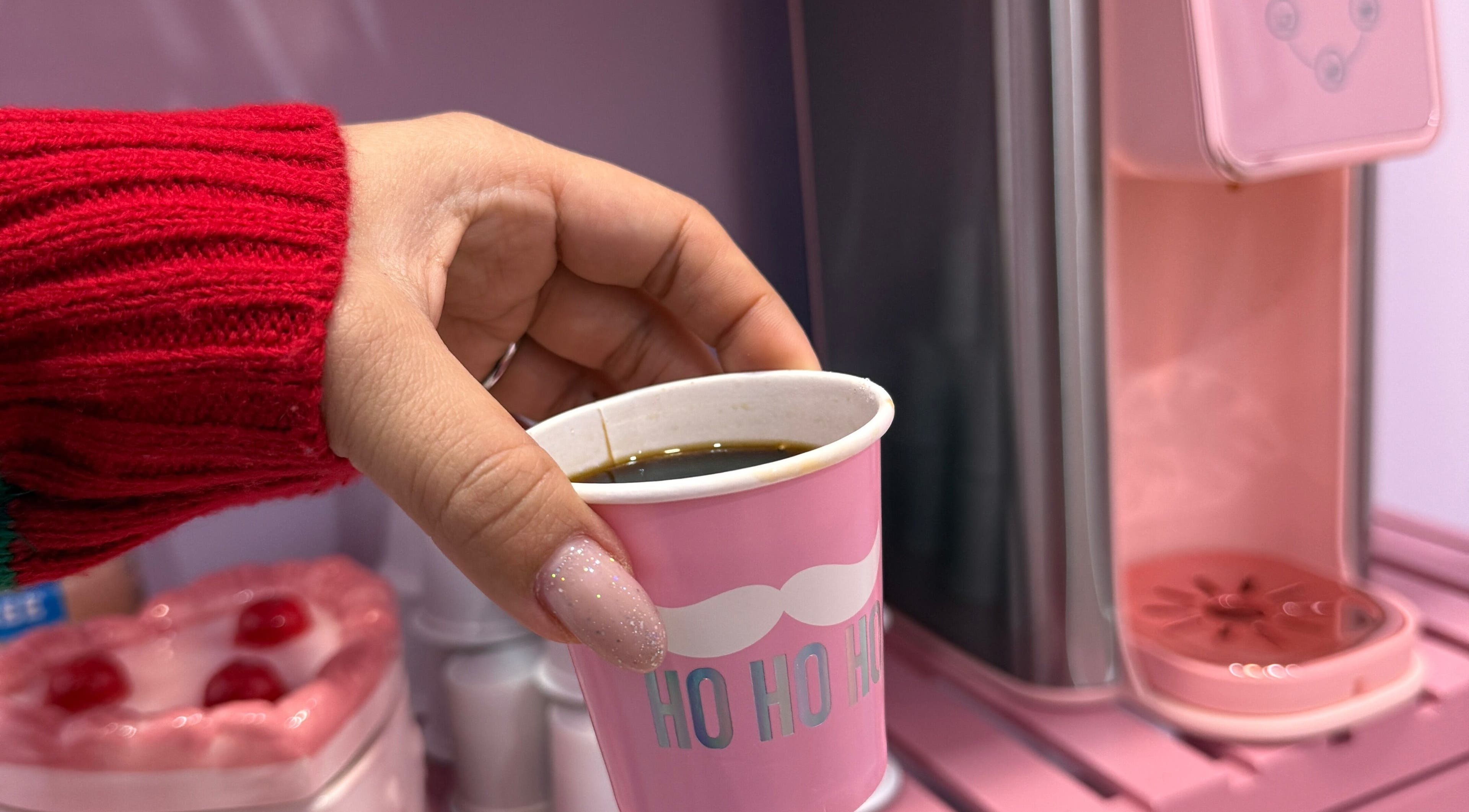Hand holding pink cup of coffee at The Nail Room, Hialeah, Florida, US, against a stylish pink background.