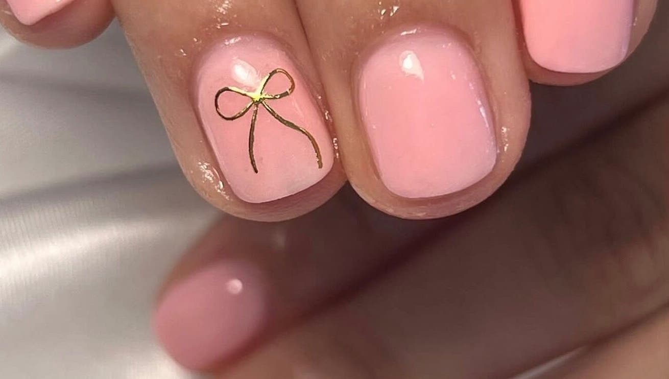Elegant pink nails with a gold bow design at Nailed It - By Vanessa, Bolton, England, GB.