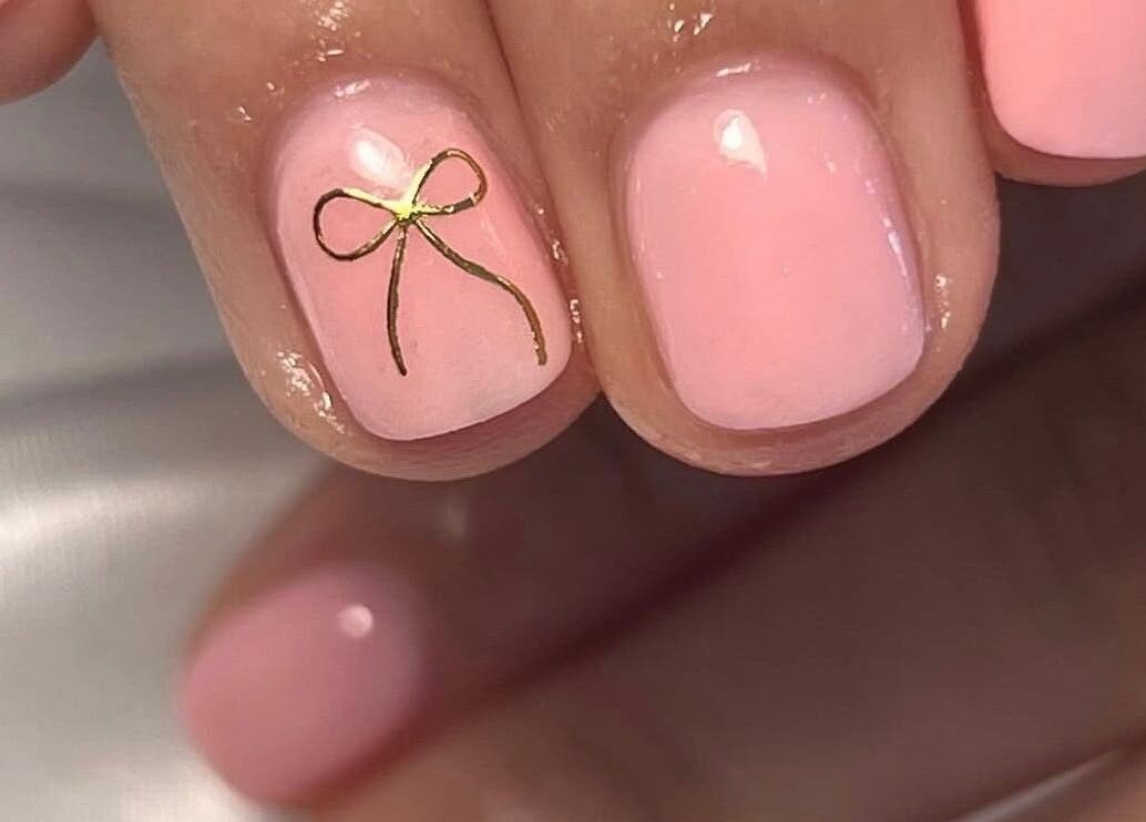 Elegant pink nails with a gold bow design at Nailed It - By Vanessa, Bolton, England, GB.
