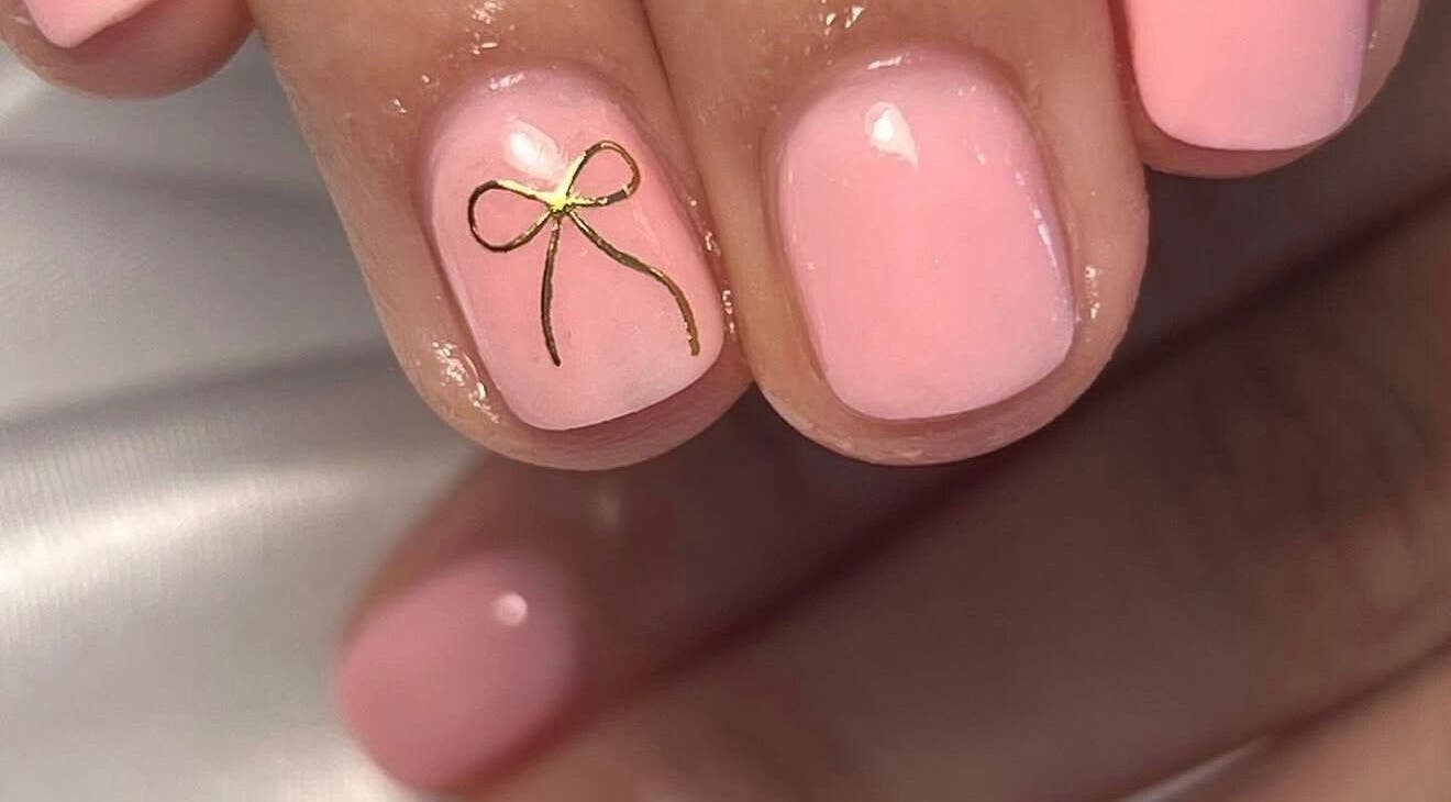 Elegant pink nails with a gold bow design at Nailed It - By Vanessa, Bolton, England, GB.