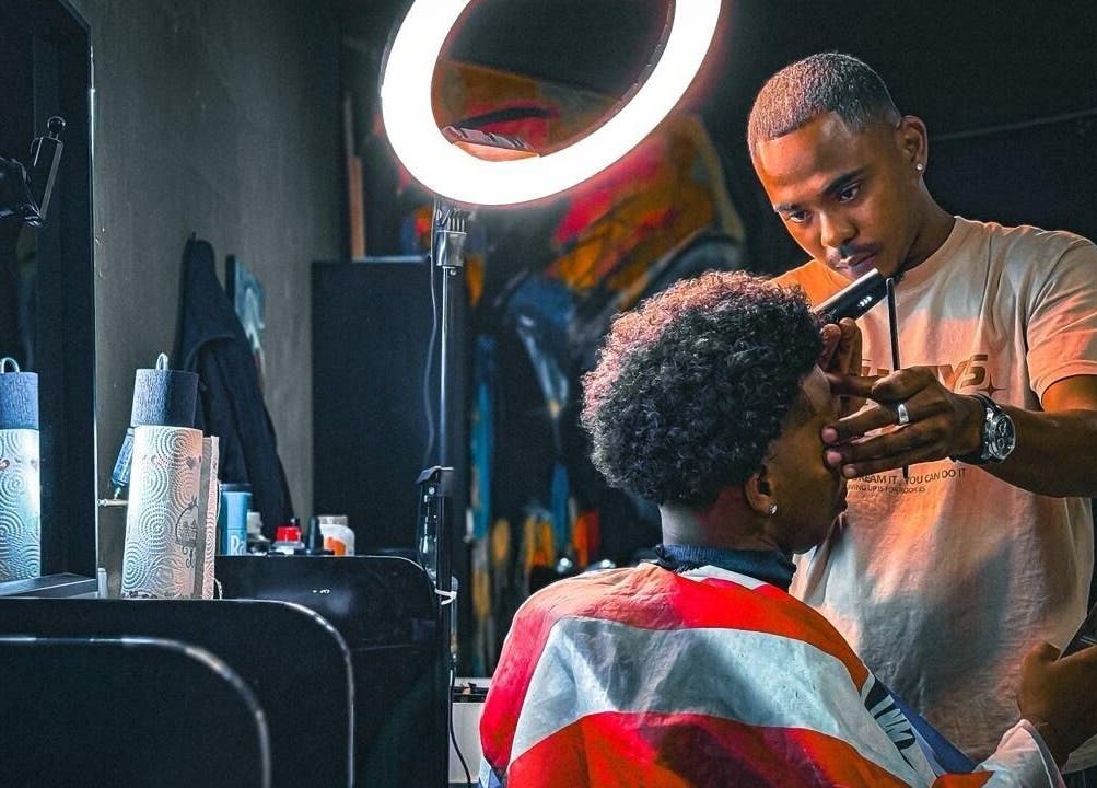 Stylist at Het Hoofd Kantoor in Paramaribo, SR, crafting a precision haircut under a ring light.