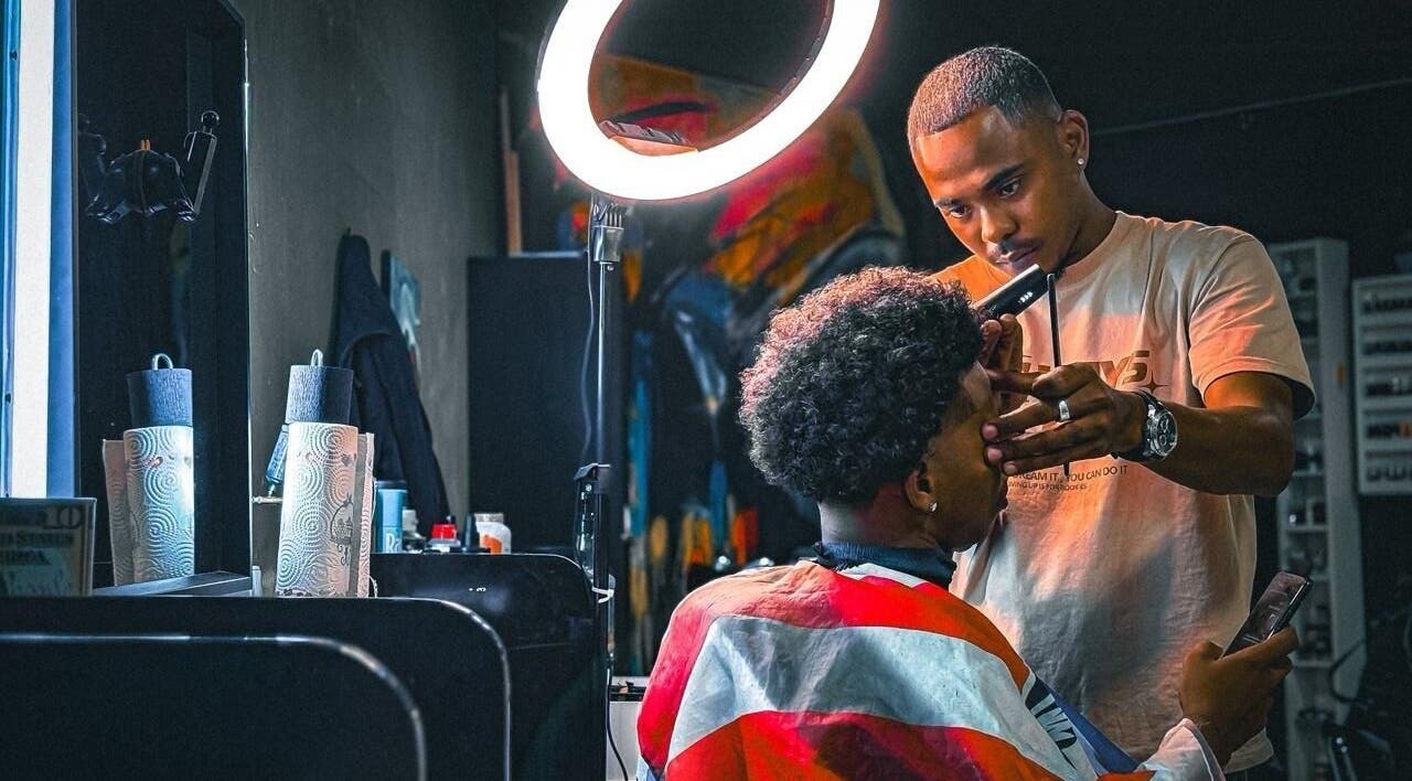 Stylist at Het Hoofd Kantoor in Paramaribo, SR, crafting a precision haircut under a ring light.