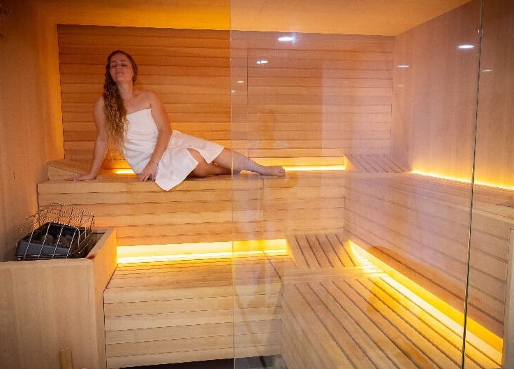 Woman relaxing in a warmly lit sauna at NECTAR Spa CLIFF, Cupecoy, SX, enjoying calming wellness ambiance.