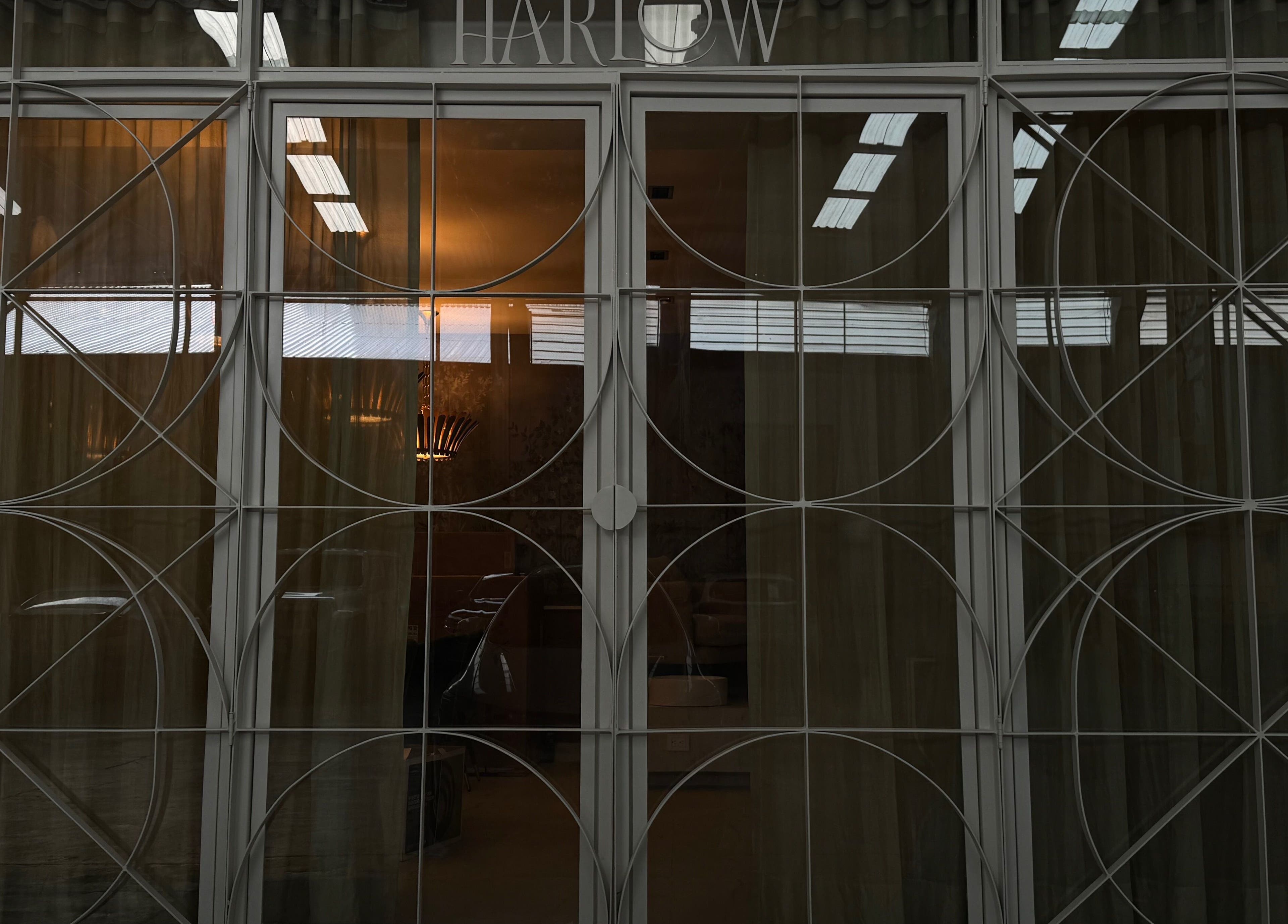 Elegant glass door at Harlow, San Pedro Garza García, Nuevo León, MX with geometric frame and glowing interior lights.