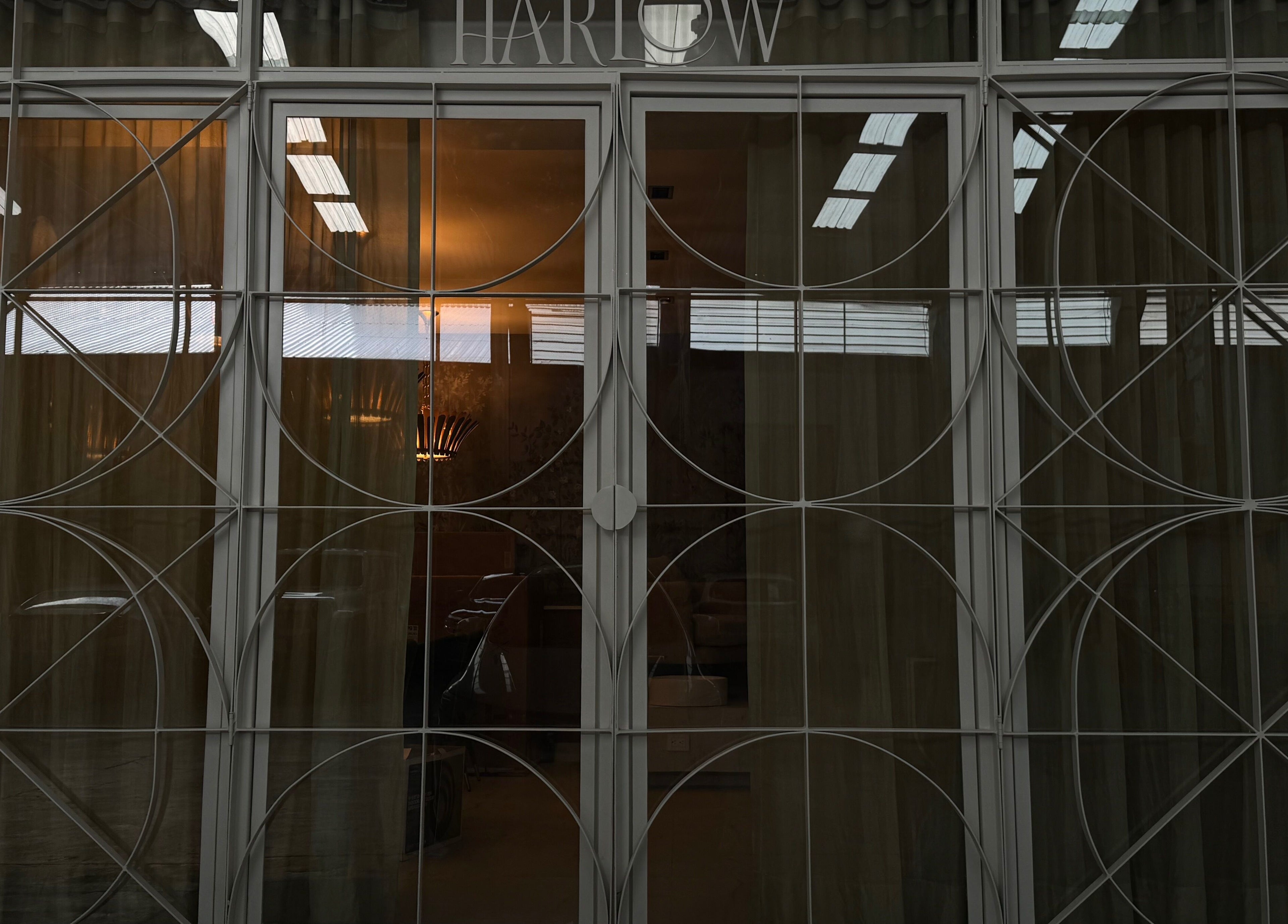 Elegant glass door at Harlow, San Pedro Garza García, Nuevo León, MX with geometric frame and glowing interior lights.
