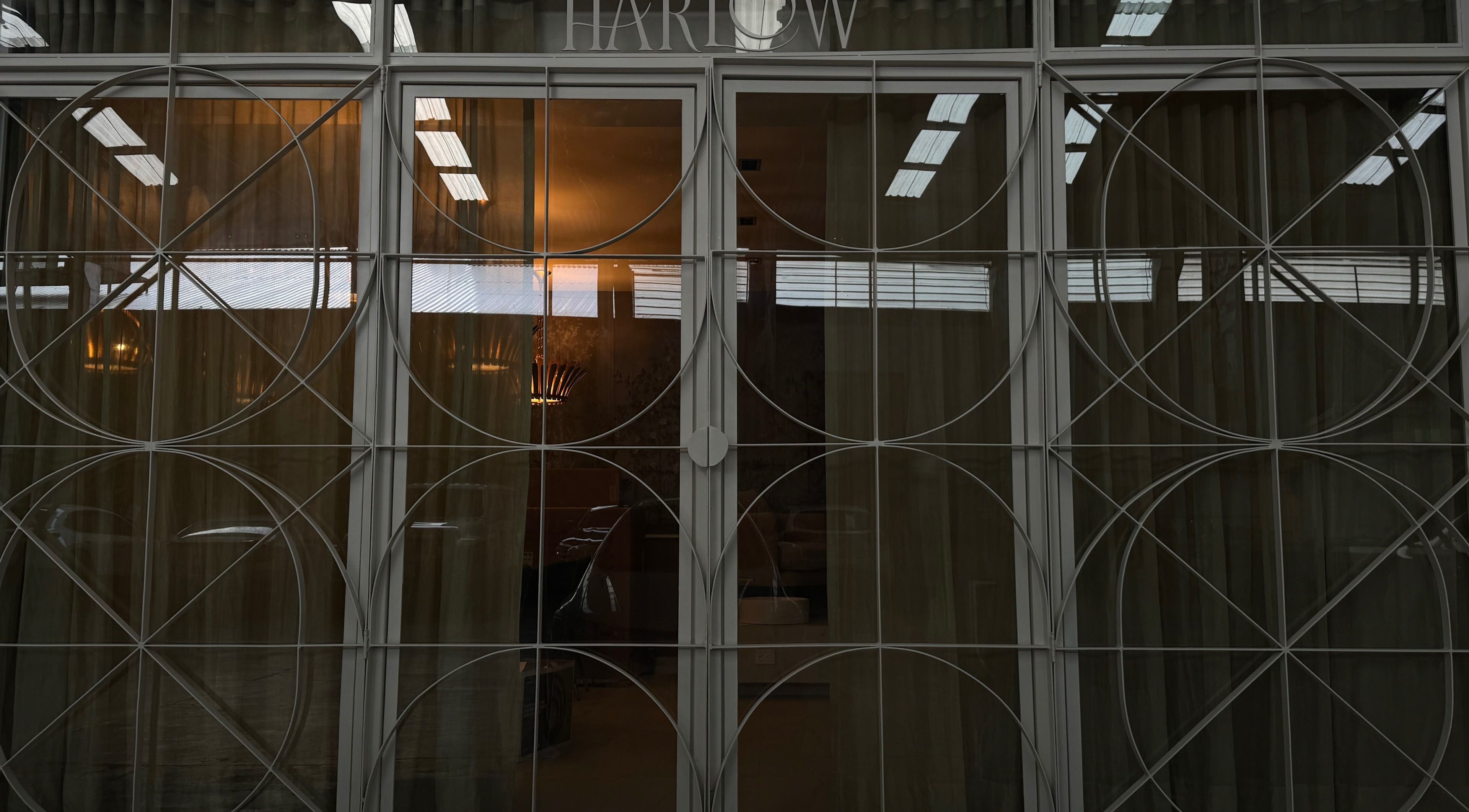 Elegant glass door at Harlow, San Pedro Garza García, Nuevo León, MX with geometric frame and glowing interior lights.