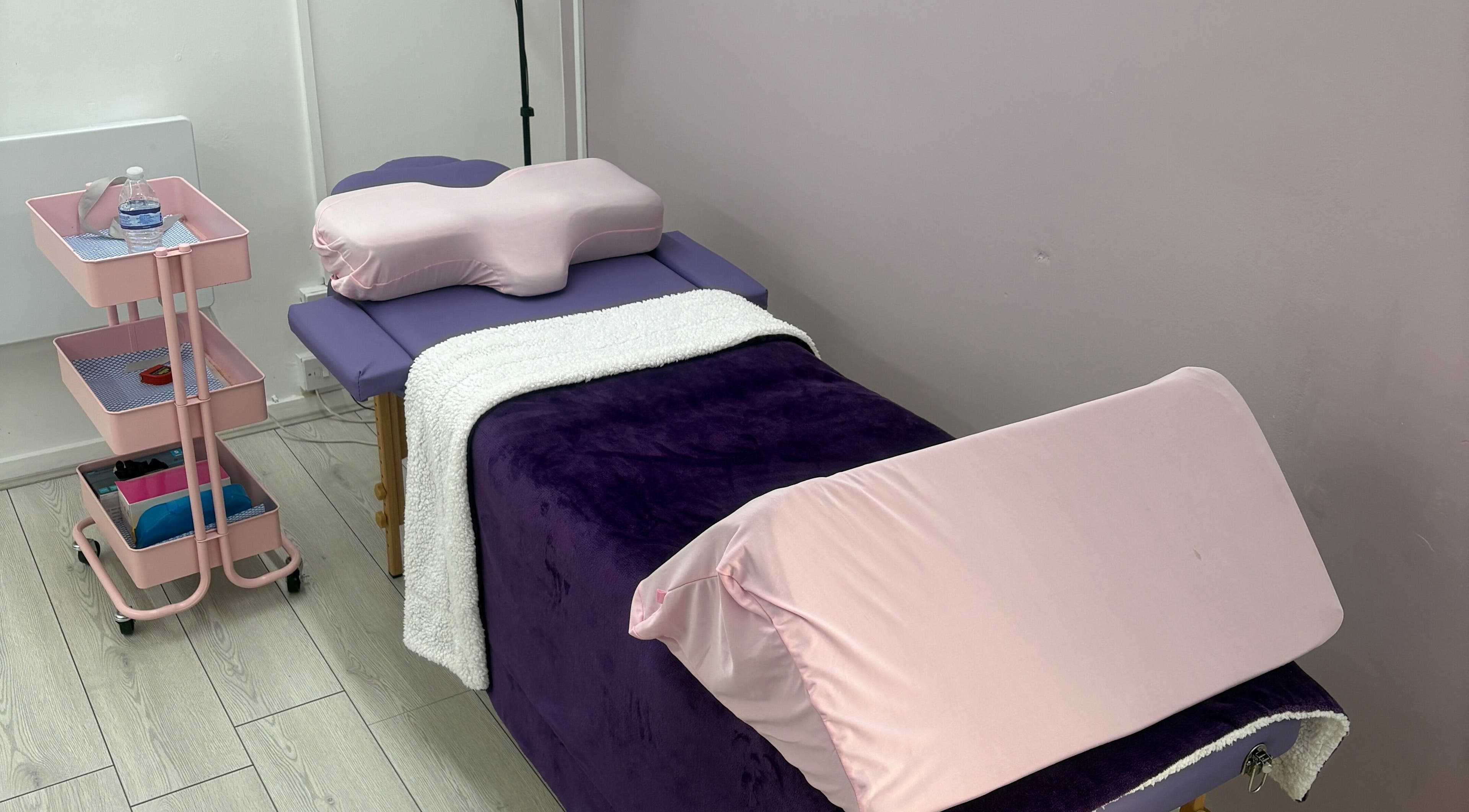 Treatment bed at Emerge Beauty Studio, Hollywood, England, GB, featuring plush purple and pink decor.