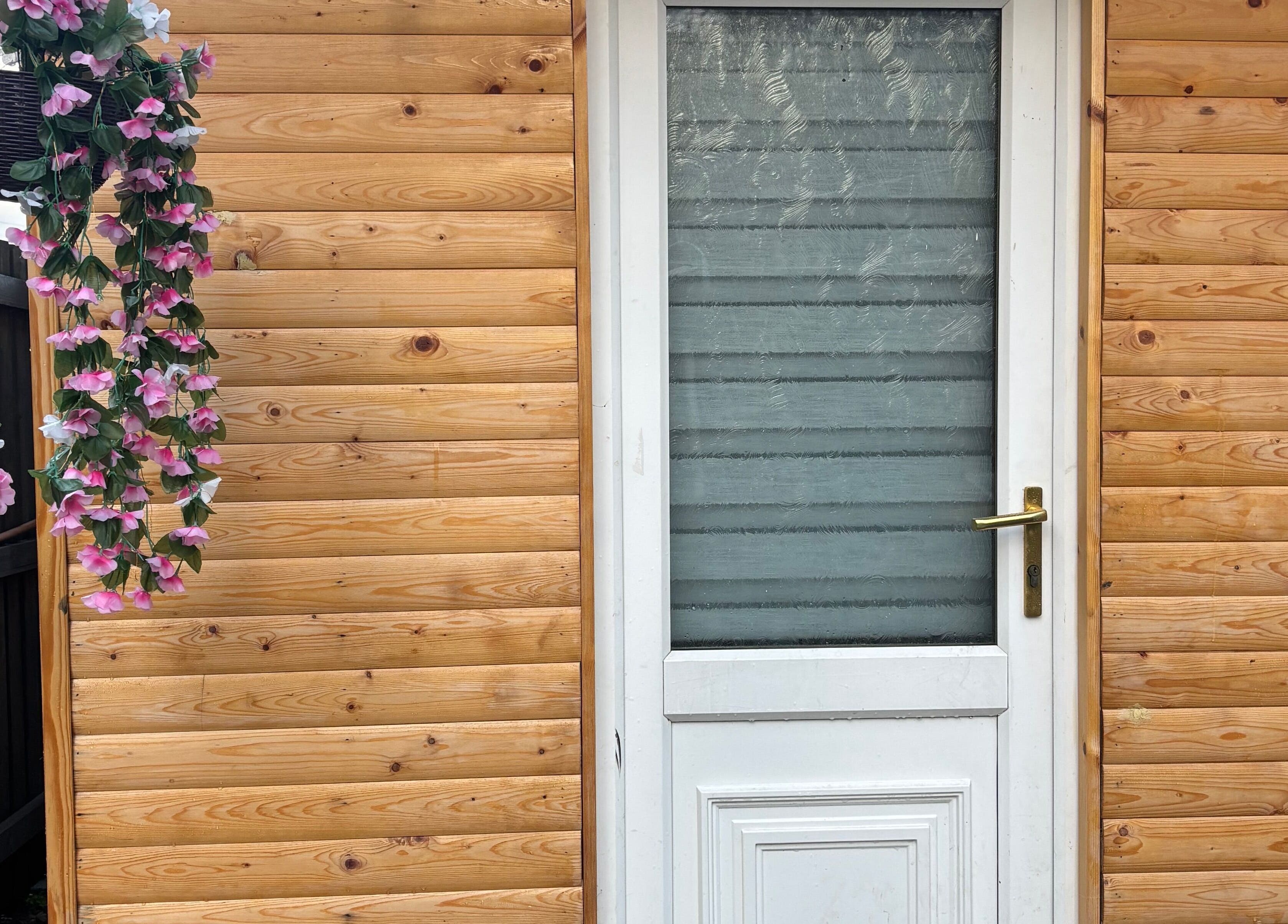 Em Beauty Care entrance with wooden facade and pink floral decor in Airdrie, Scotland, GB.