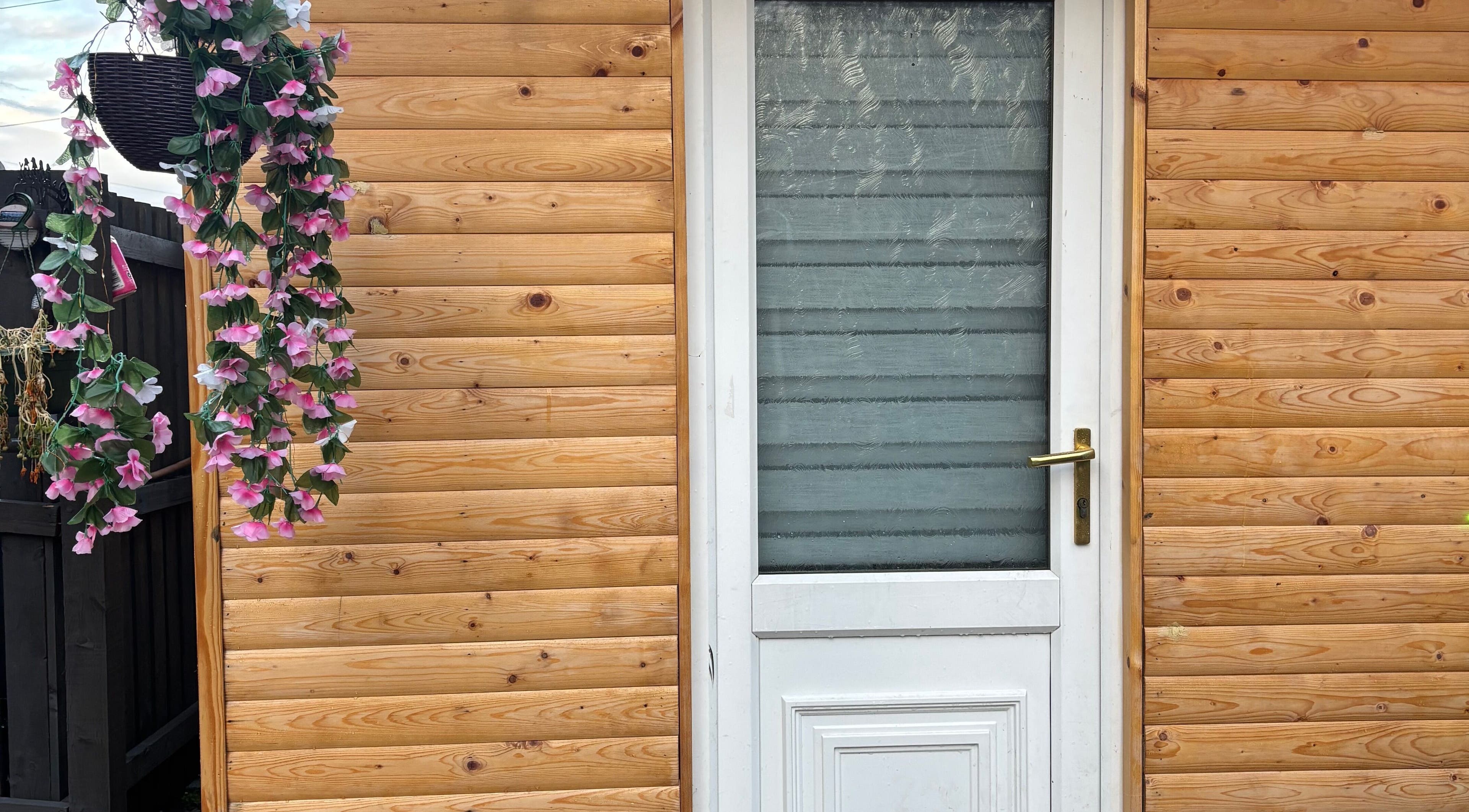 Em Beauty Care entrance with wooden facade and pink floral decor in Airdrie, Scotland, GB.