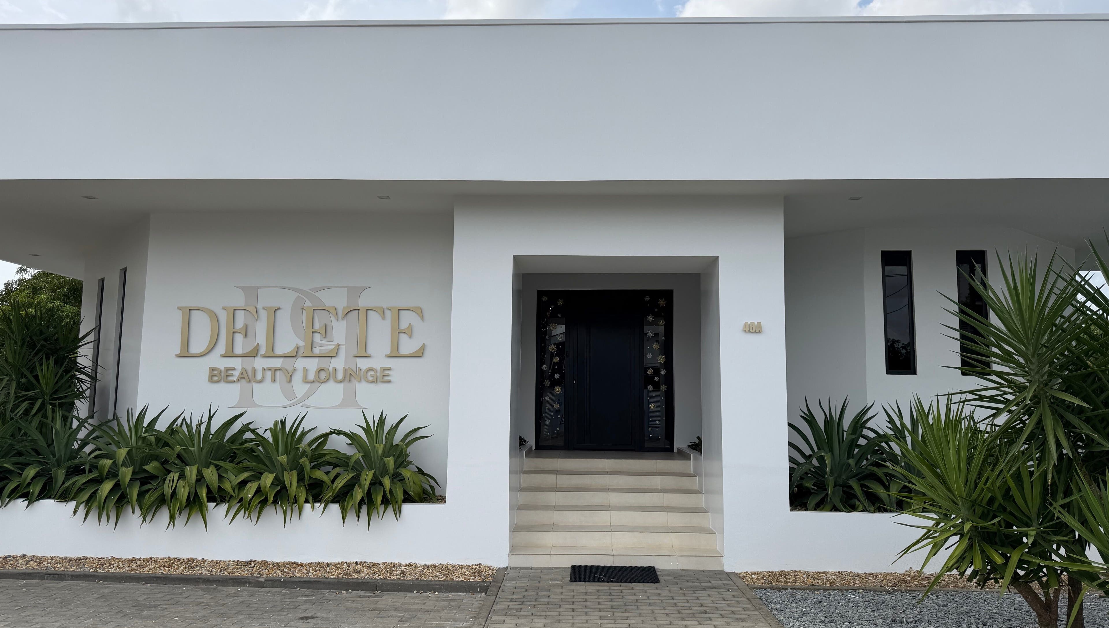 Entrance of Delete Beauty Lounge, Paramaribo, Paramaribo, SR with sleek white exterior and lush greenery.