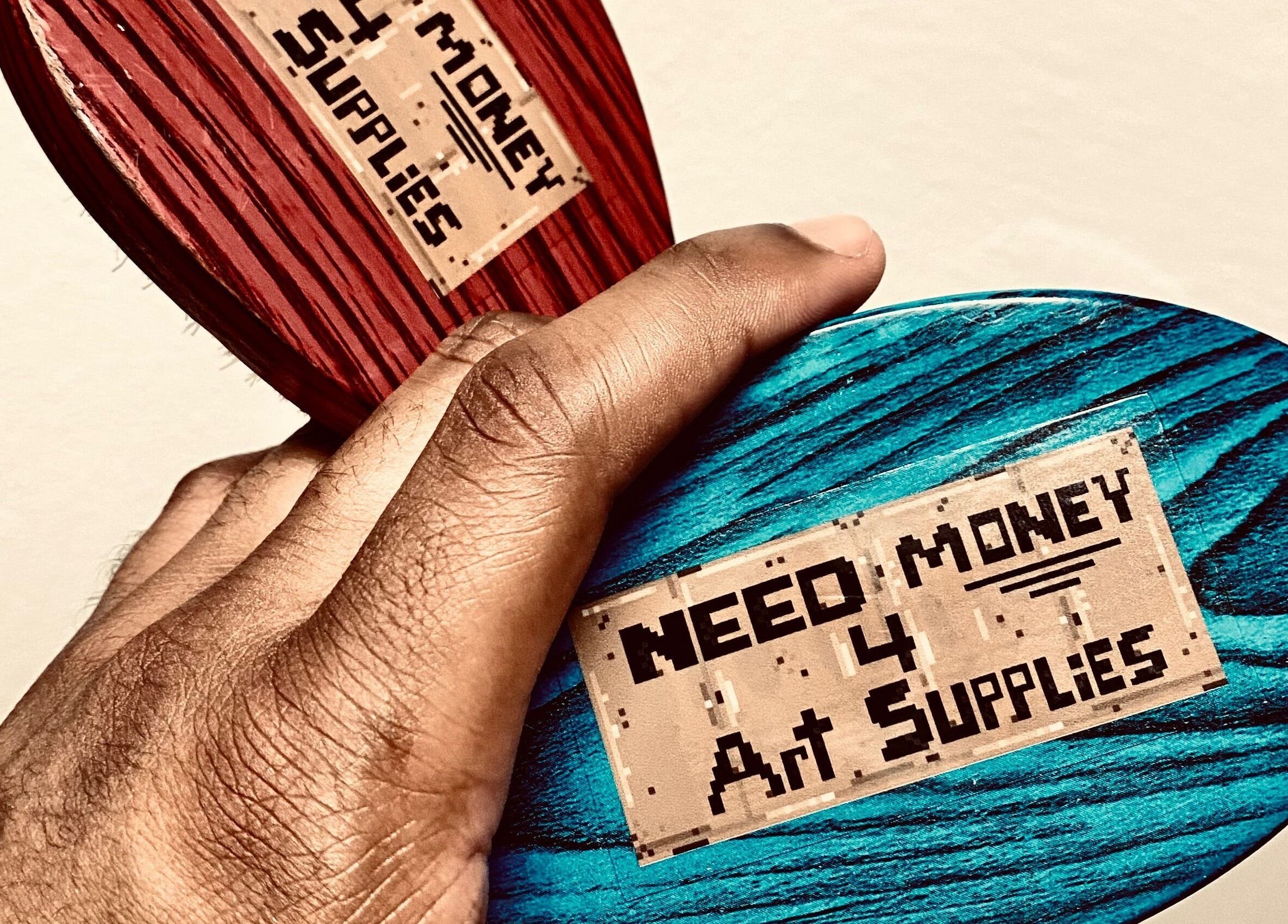 Creative design with 'Need Money 4 Art Supplies' held on colored wood at BONE | BARBER + SMP, Spring, Texas, US.
