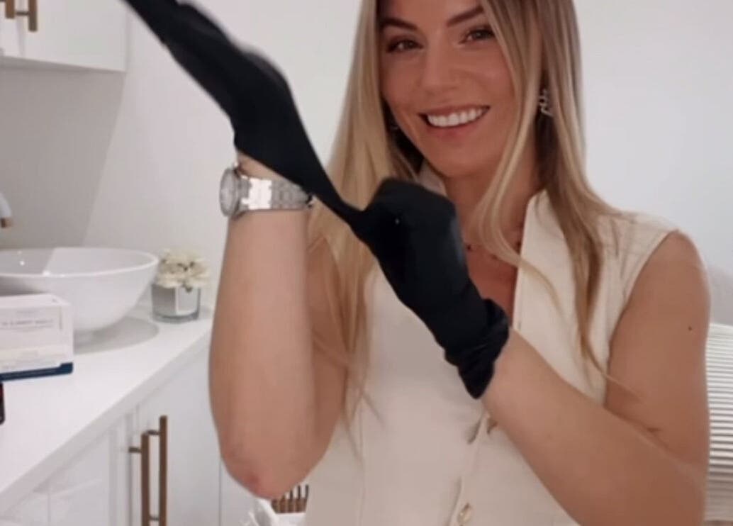 Smiling beautician at Aura Skinn By Sandra, Buckhurst Hill, England, GB putting on gloves in a bright treatment room.