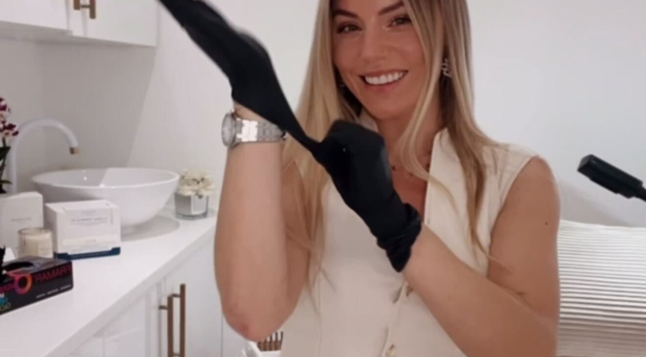 Smiling beautician at Aura Skinn By Sandra, Buckhurst Hill, England, GB putting on gloves in a bright treatment room.