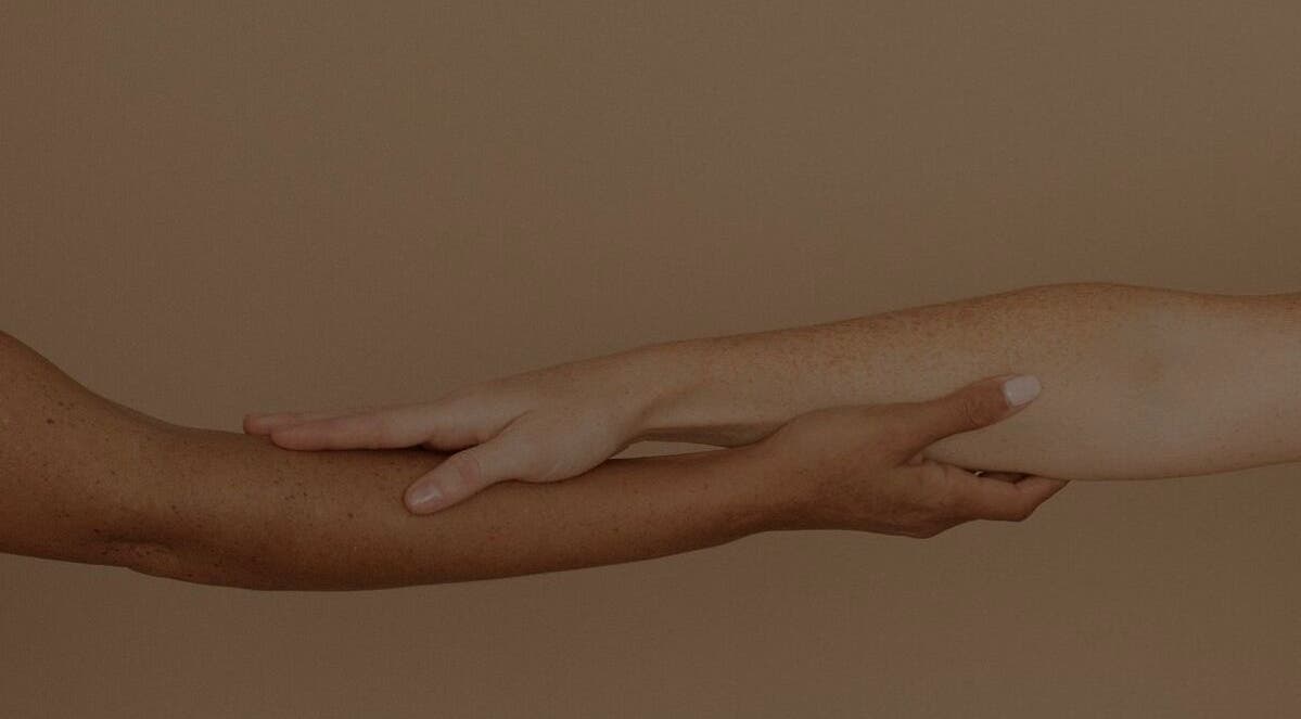 Two diverse hands gently touch at Sculpt Studio, CA, symbolizing unity and wellness.