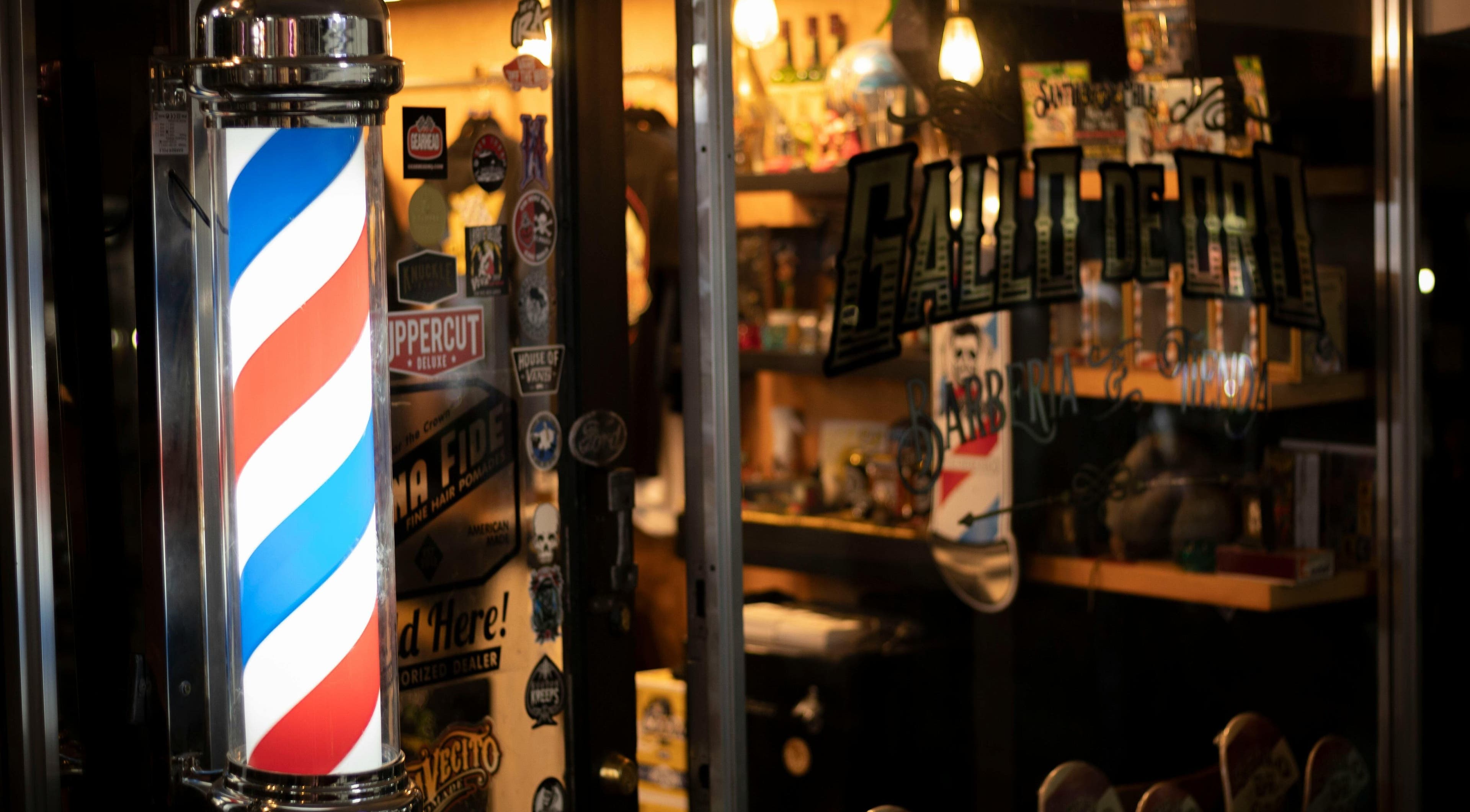 Entrada iluminada de BarberyandBeauty CR en Aserri, San José, con poste de barbería clásico.