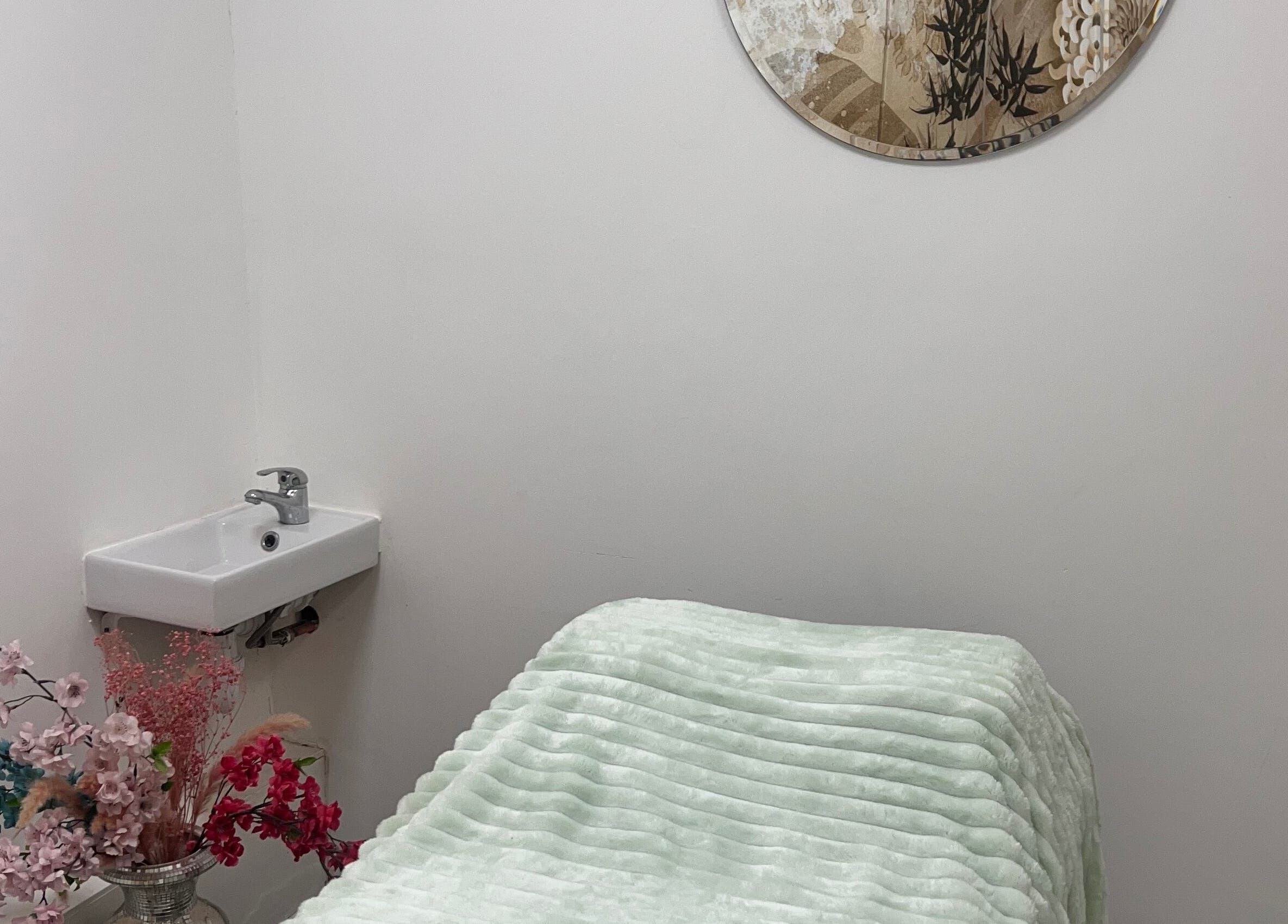 Tranquil massage room at Gaia Massage, Harrow, England, GB. Cozy bed with floral decor and modern sink.
