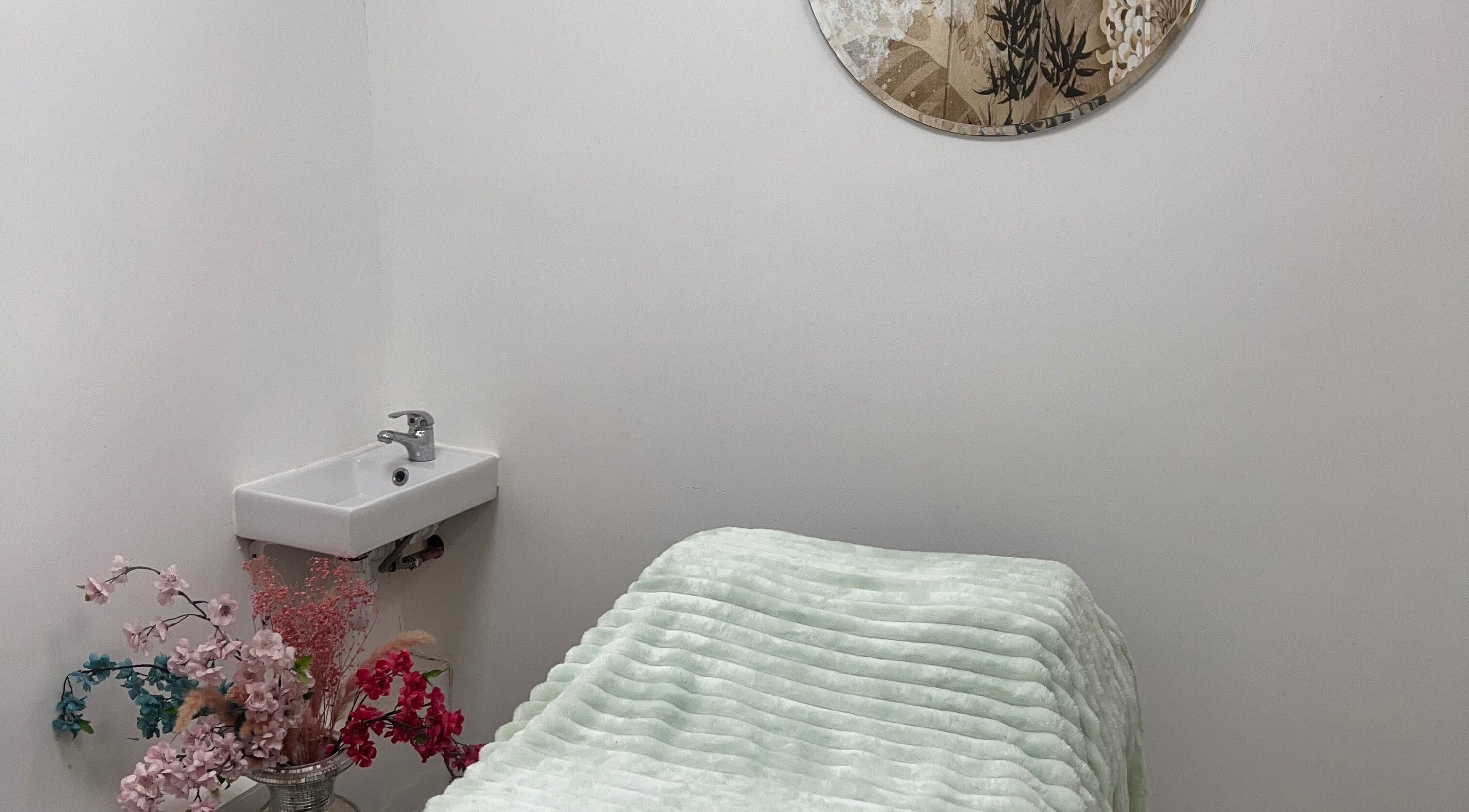 Tranquil massage room at Gaia Massage, Harrow, England, GB. Cozy bed with floral decor and modern sink.