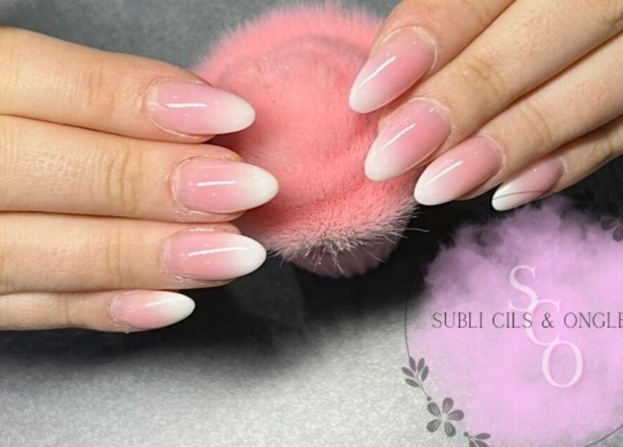 Ongles en gel rose et blanc chez Subli Cils & Ongles, Gouvieux, Hauts-de-France, FR, sur une surface grise.