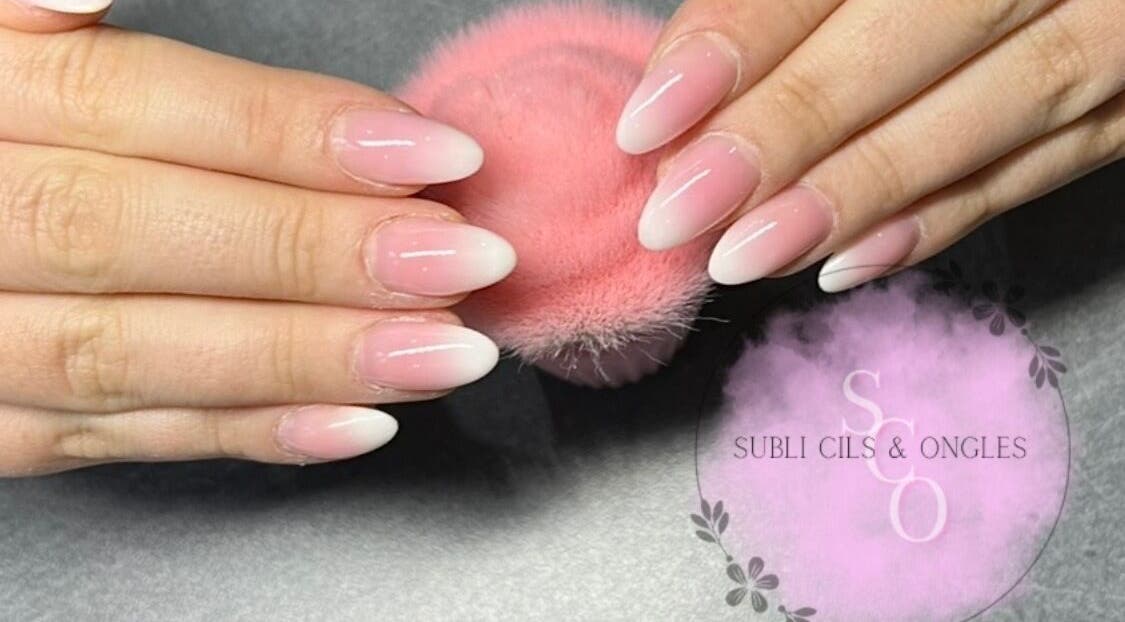 Ongles en gel rose et blanc chez Subli Cils & Ongles, Gouvieux, Hauts-de-France, FR, sur une surface grise.