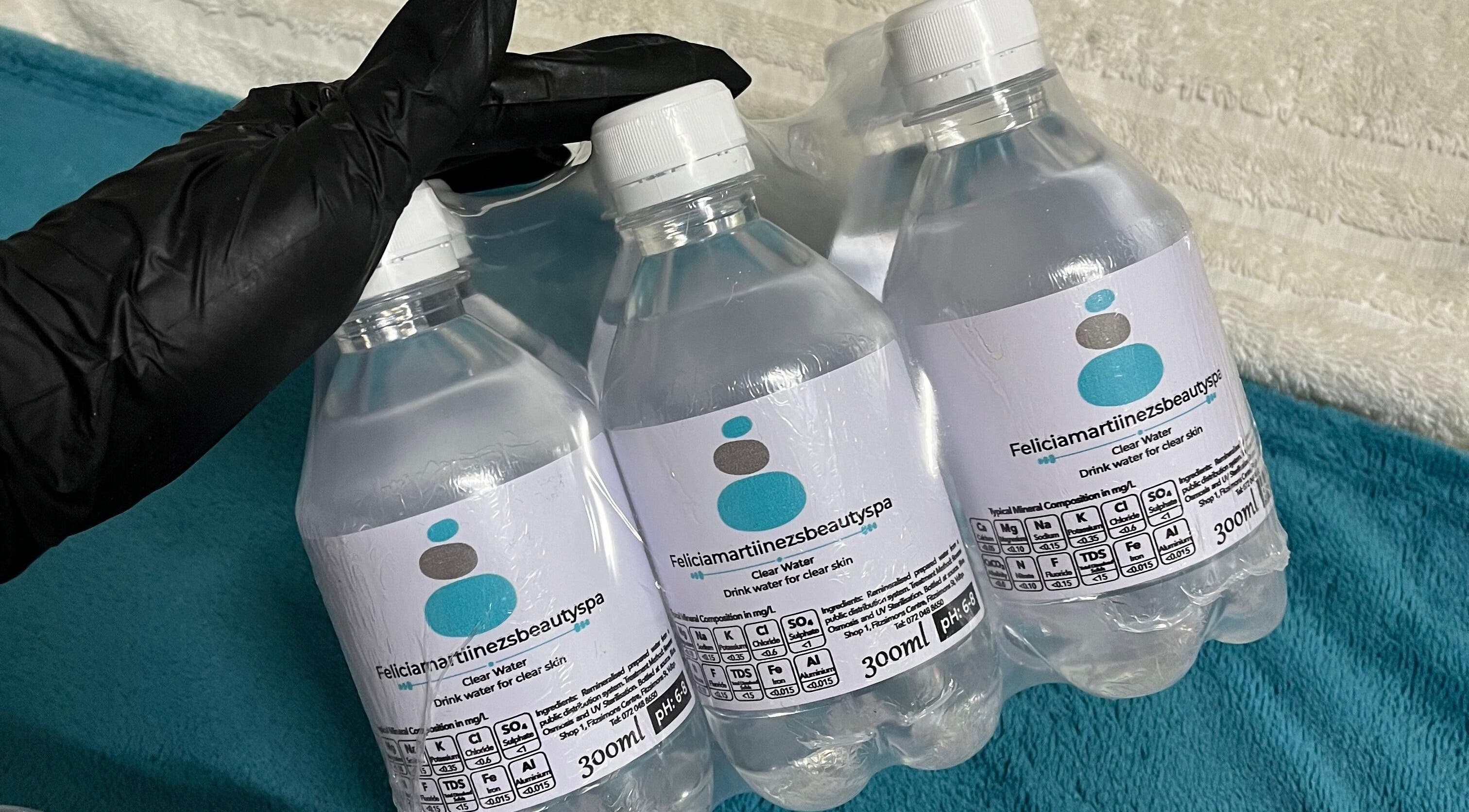 Bottled water branded with Felicia.ciamartiinezsbeautyspa, Vanderbijlpark, Gauteng, ZA, on a blue surface.