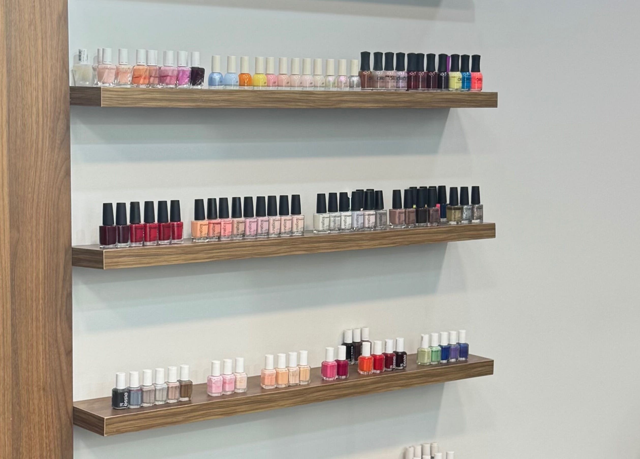 A variety of vibrant nail polishes on elegant wooden shelves at Ameeri Touch Hair & Beauty, Bu Quwah, BH.