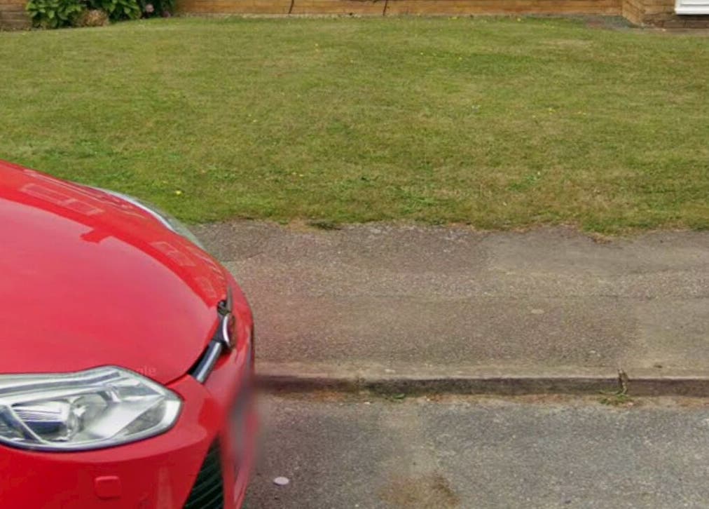 A vibrant red car parked outside NailsbyNays in Hitchin, England, GB, in front of a lush green lawn.