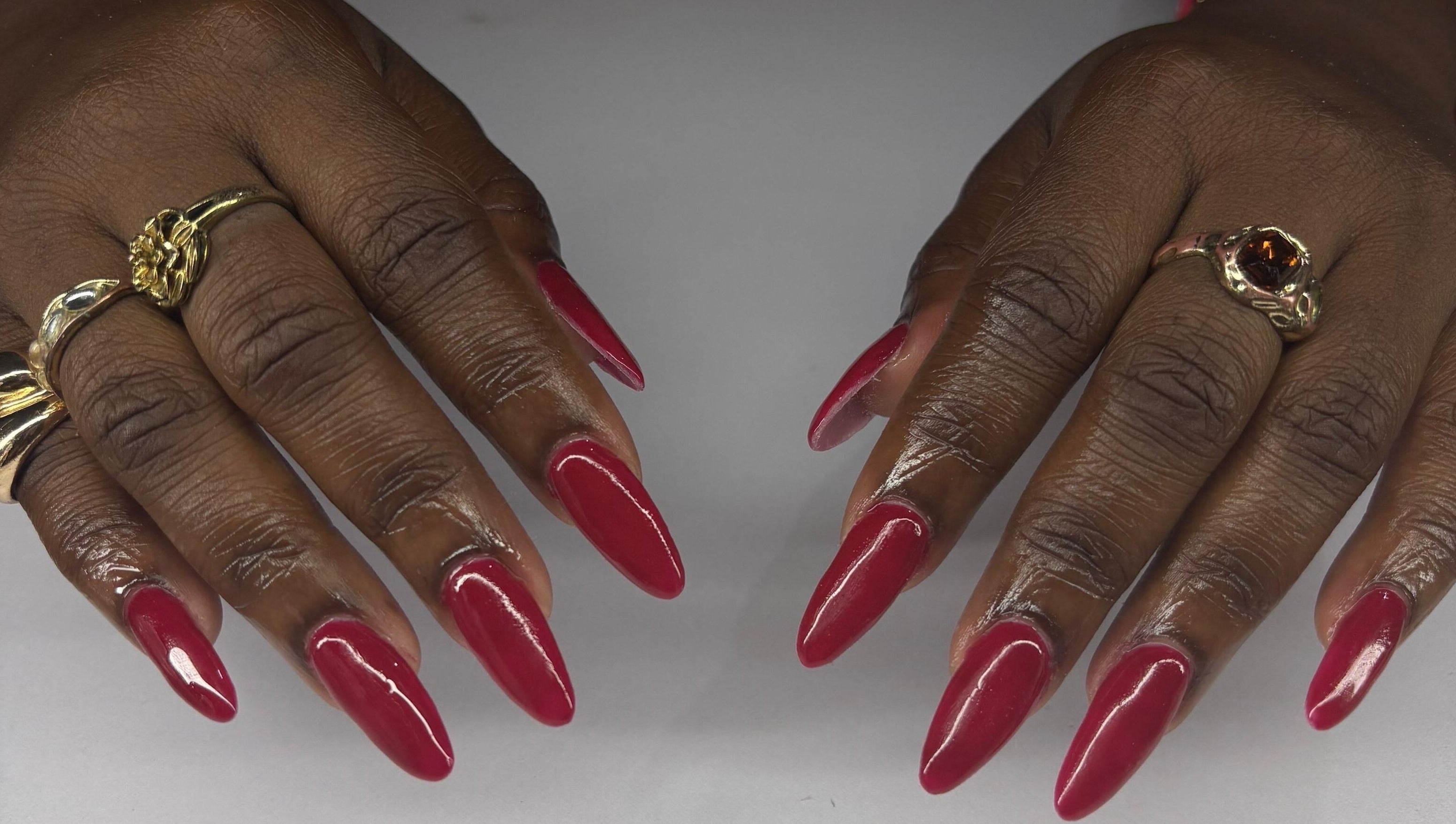 Stylish red manicure at True Beauty, Charlotte, Charlotte, VC with intricate golden rings displayed.
