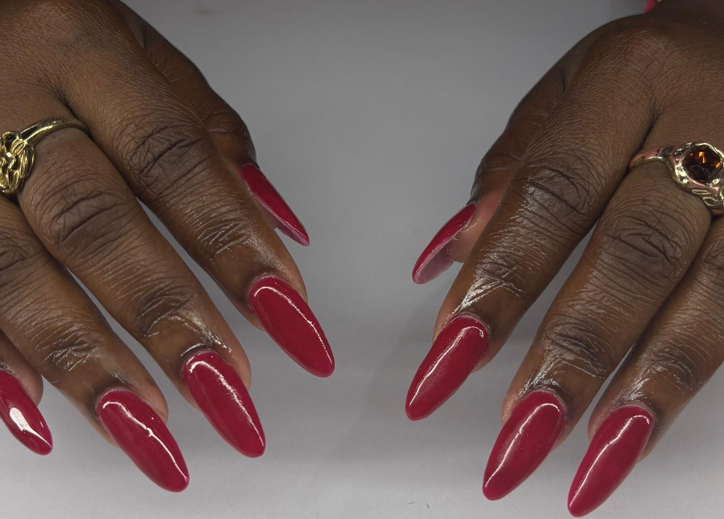 Stylish red manicure at True Beauty, Charlotte, Charlotte, VC with intricate golden rings displayed.