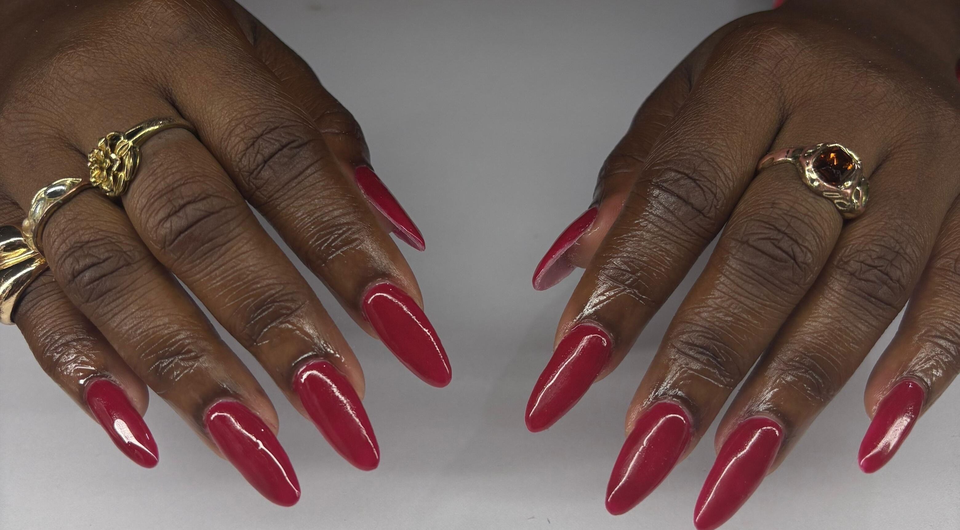 Stylish red manicure at True Beauty, Charlotte, Charlotte, VC with intricate golden rings displayed.