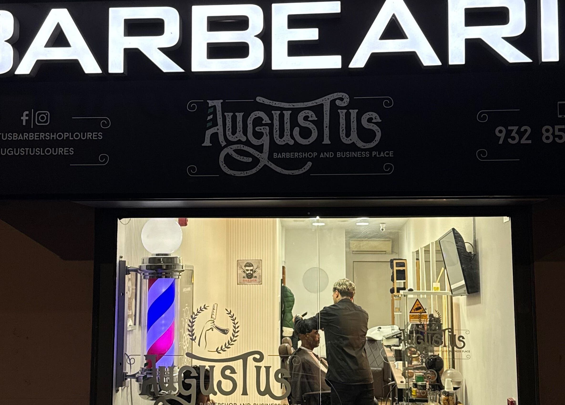 Exterior iluminado da Barbearia Augustus Loures, Loures, Lisboa, PT, com barbeiro em ação.