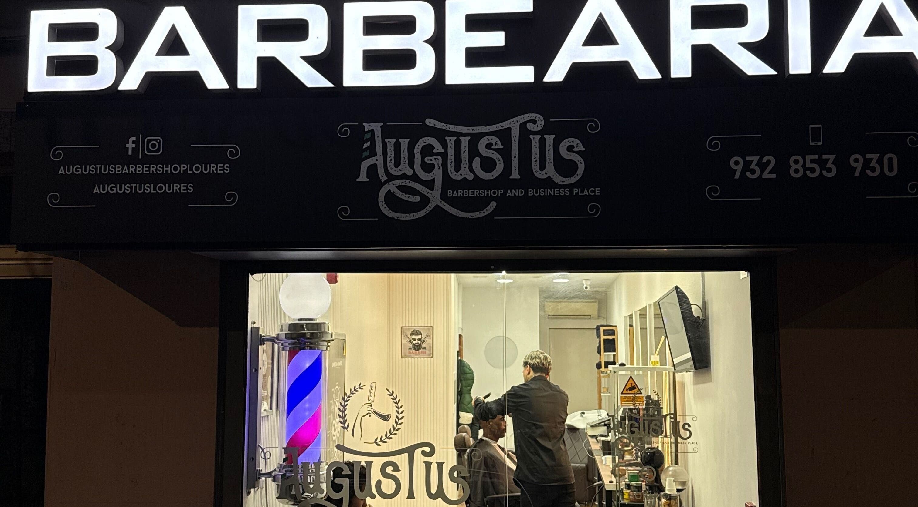 Exterior iluminado da Barbearia Augustus Loures, Loures, Lisboa, PT, com barbeiro em ação.