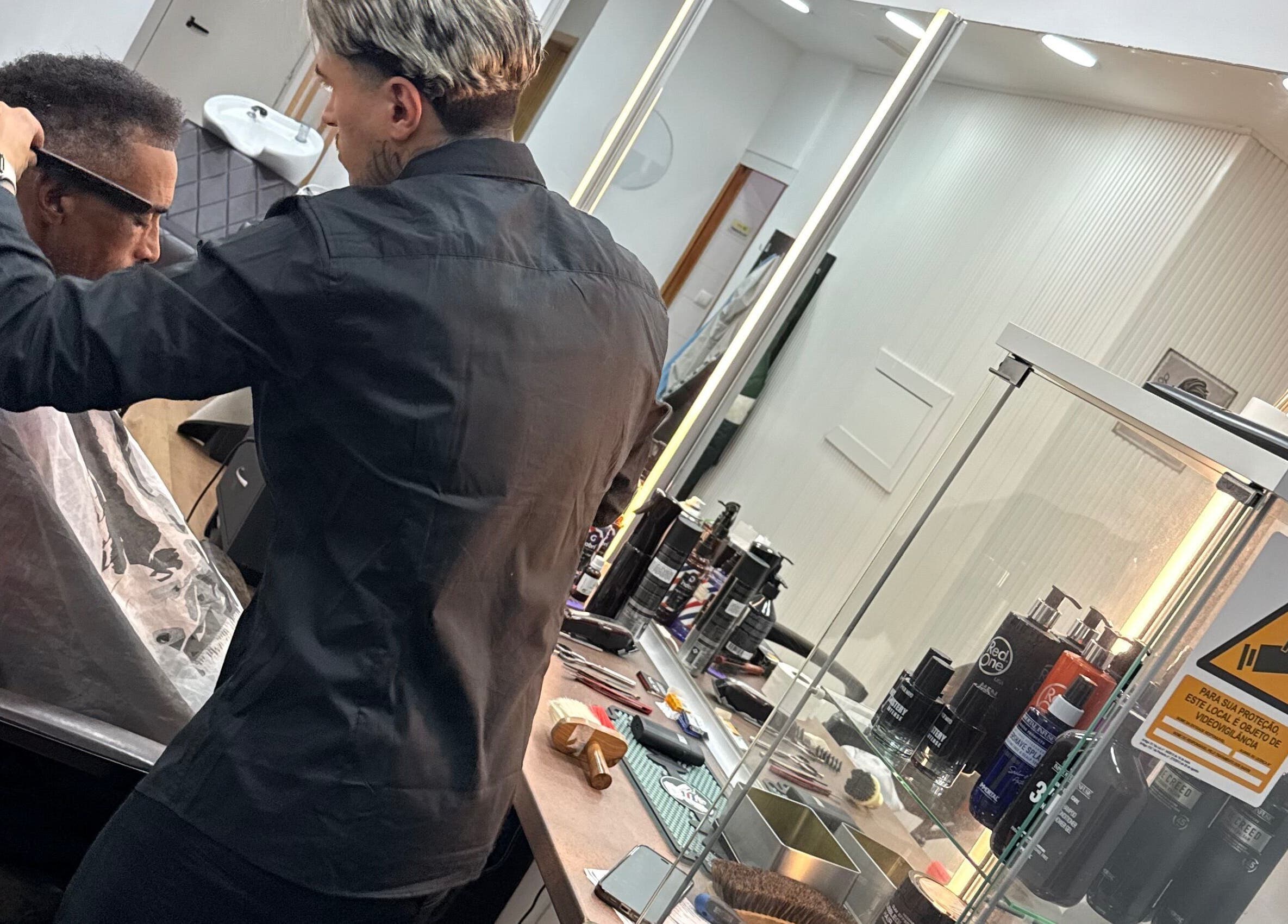 Barbeiro atende cliente em Barbearia Augustus Loures, Loures, Lisboa, PT, refletido em espelhos iluminados.