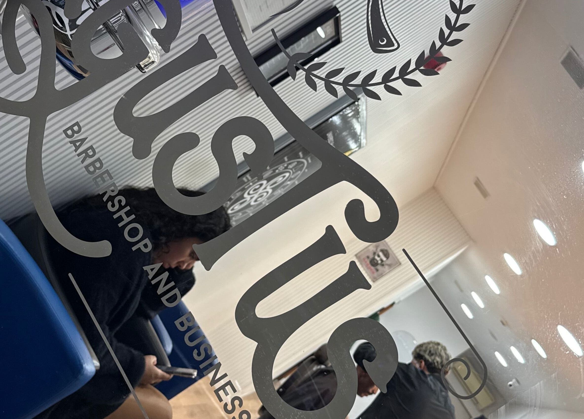 Interior da Barbearia Augustus Loures em Loures, Lisboa, PT, refletido em vidro com cadeiras azuis.