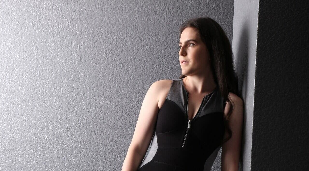 A thoughtful woman in activewear leans on a wall at Coaching with Amy, Chirk, Wales, GB.