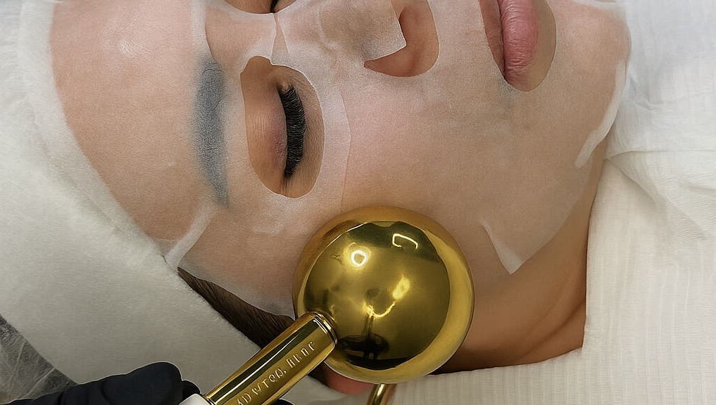 Luxury facial treatment at Oseas Beauty & Spa in Tampa, Florida, US, featuring a gold roller and sheet mask.