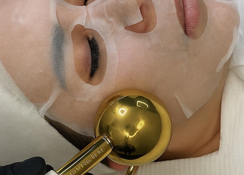 Luxury facial treatment at Oseas Beauty & Spa in Tampa, Florida, US, featuring a gold roller and sheet mask.