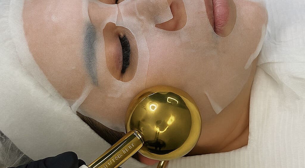 Luxury facial treatment at Oseas Beauty & Spa in Tampa, Florida, US, featuring a gold roller and sheet mask.