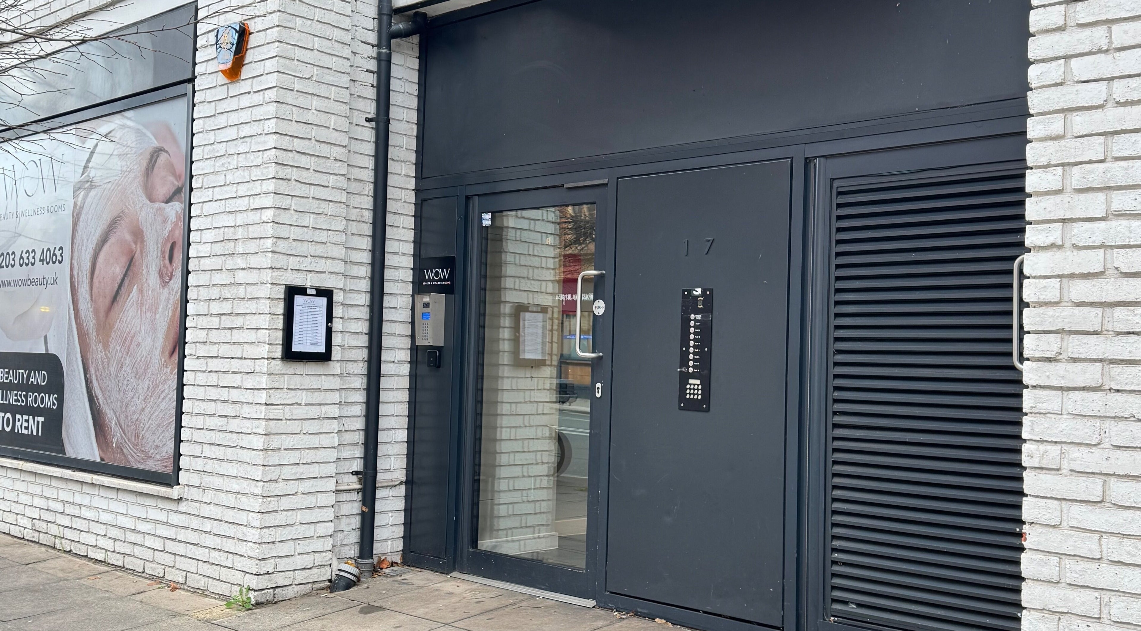 Entrance of Elya Aesthetic, London, England, GB. Modern black door and signage against white brick wall.