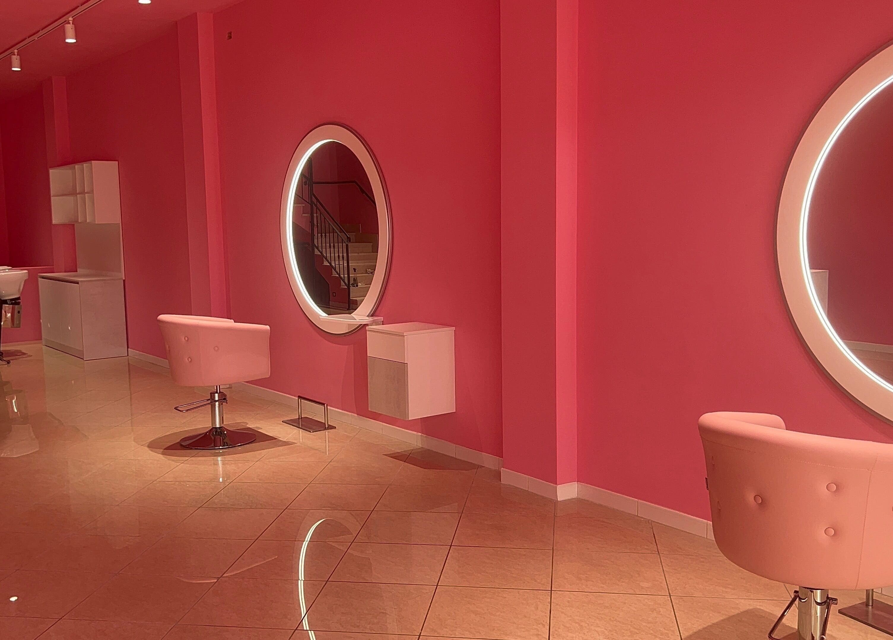 Interno di THE BARBER WOMAN a Sava, Puglia, IT; pareti rosa con specchi rotondi illuminati.