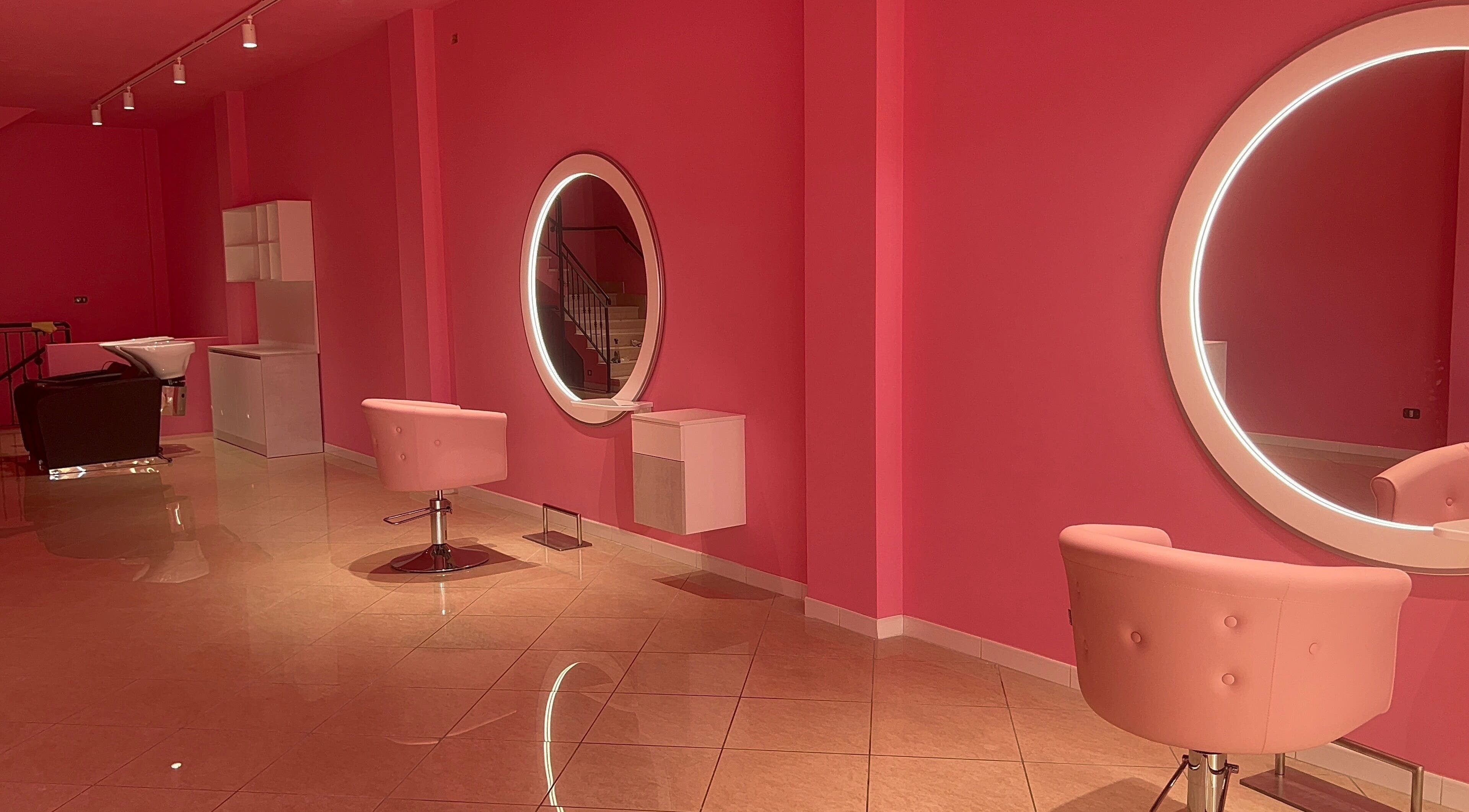 Interno moderno di salone rosa a The Barber Woman, Sava, Puglia, IT con specchi circolari e sedie chic.