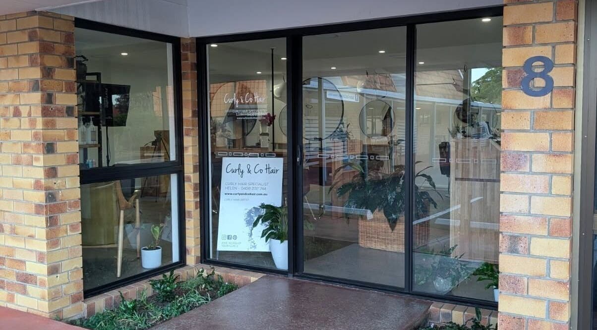 Front view of Curly & Co Hair salon in Tweed Heads, NSW, AU, showcasing modern glass door and signage.