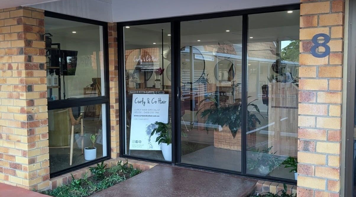 Exterior of Curly & Co Hair in Tweed Heads, New South Wales, AU showcasing modern glass facade and welcoming atmosphere.