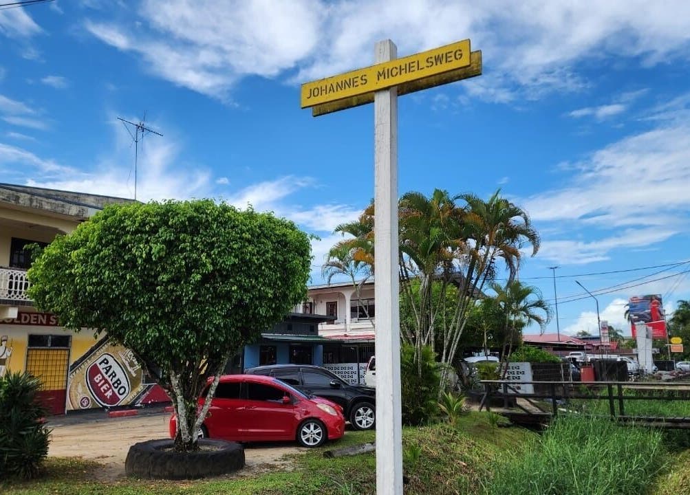 Street view near Raoef's Barbershop, Nieuwe Grond, Wanica, SR, with a vibrant tree and colorful buildings.